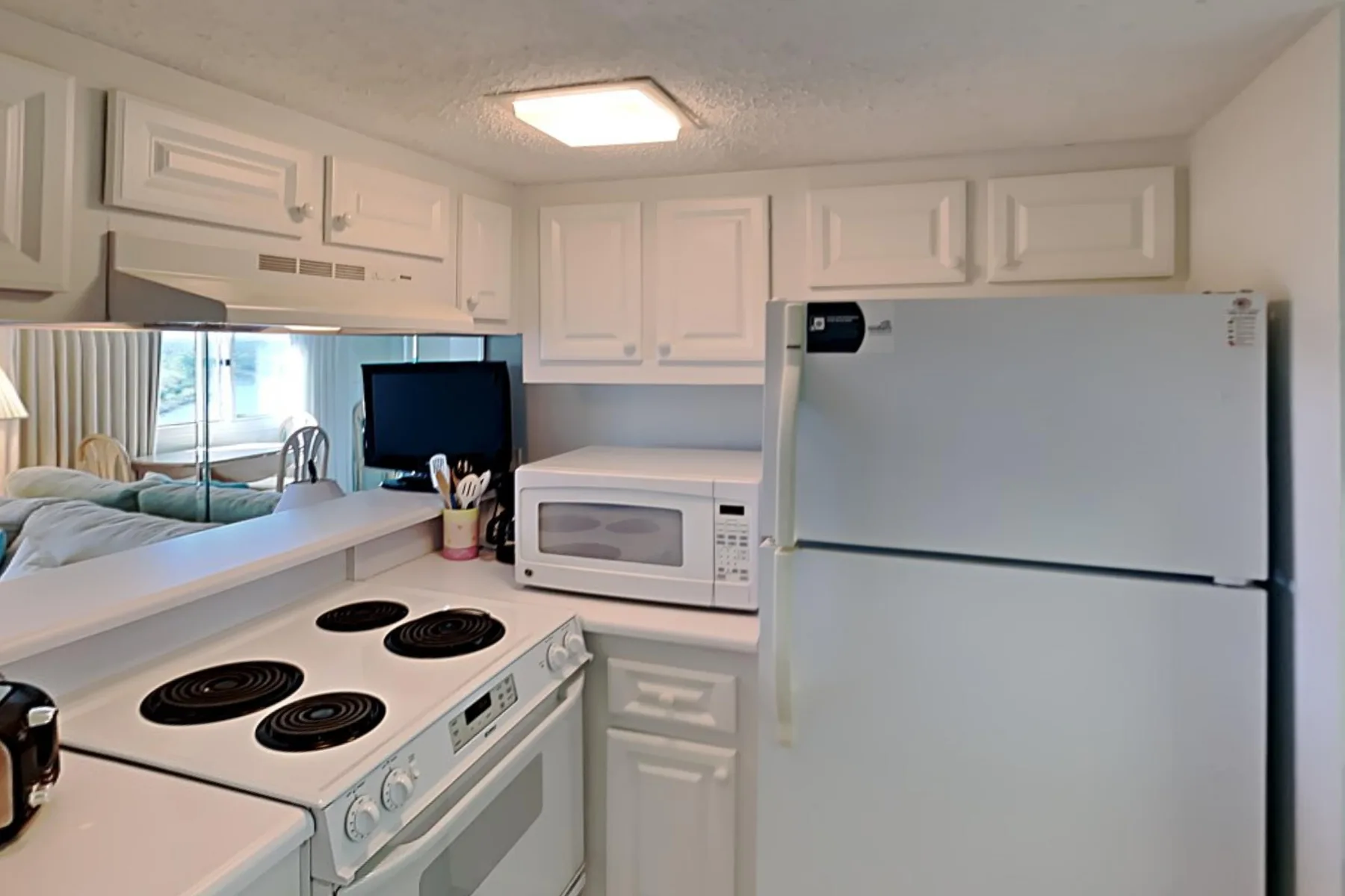Una cocina compacta con gabinetes blancos, estufa, microondas y refrigerador.
