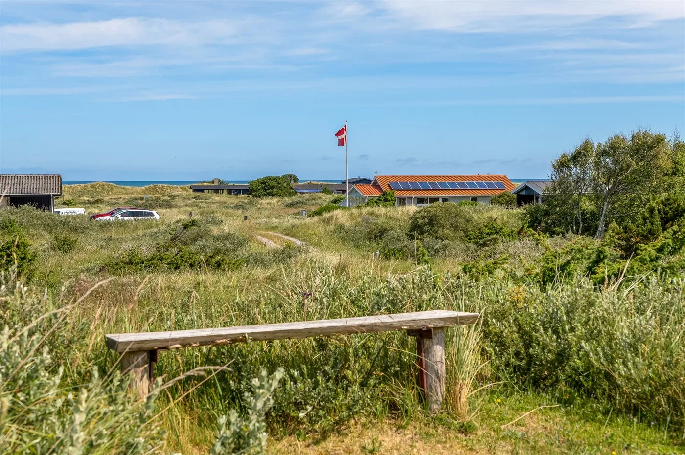 Un paisaje costero con hierba, edificios bajos y el mar visible a lo lejos.