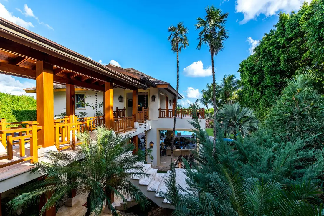 A tropical building with wooden balconies is surrounded by lush greenery and palm trees.