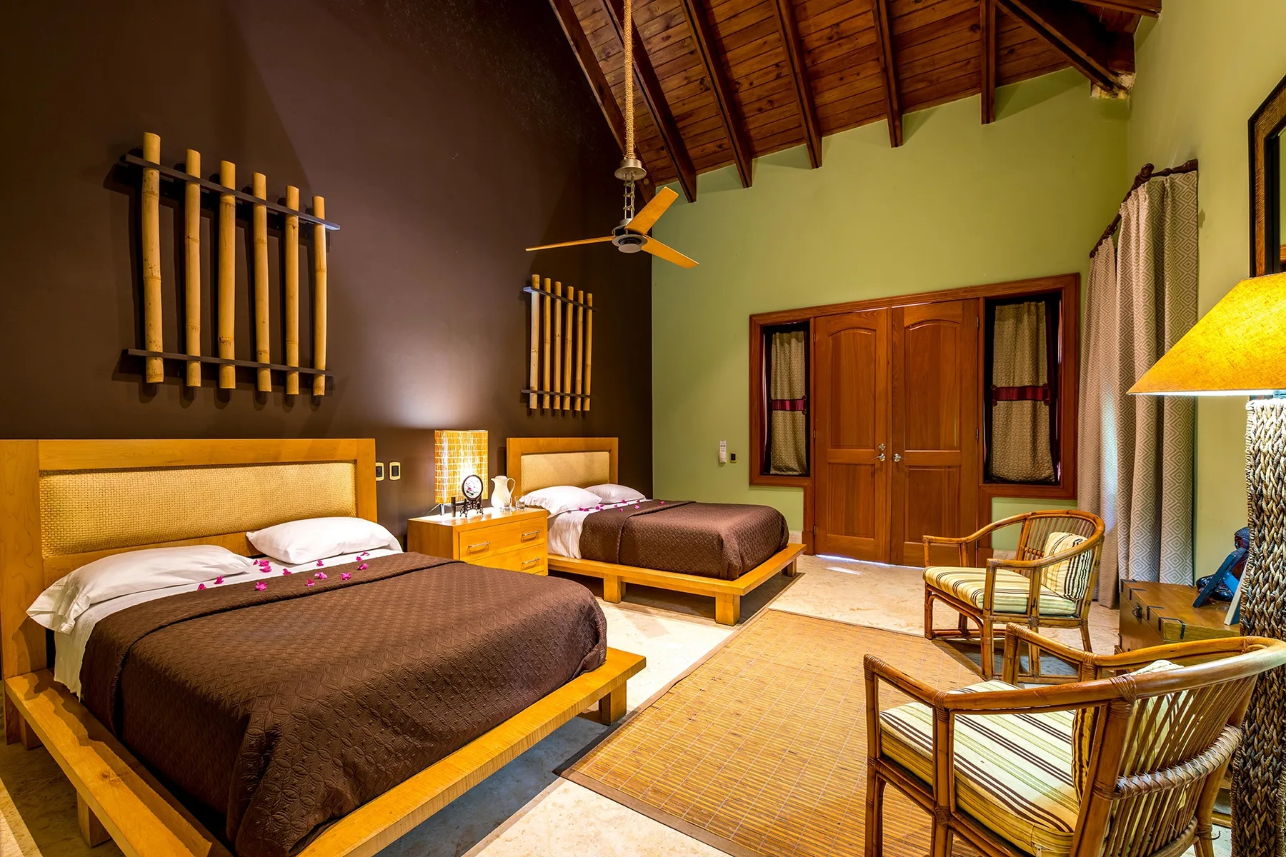 A bedroom with two beds, a small table, and woven seating.