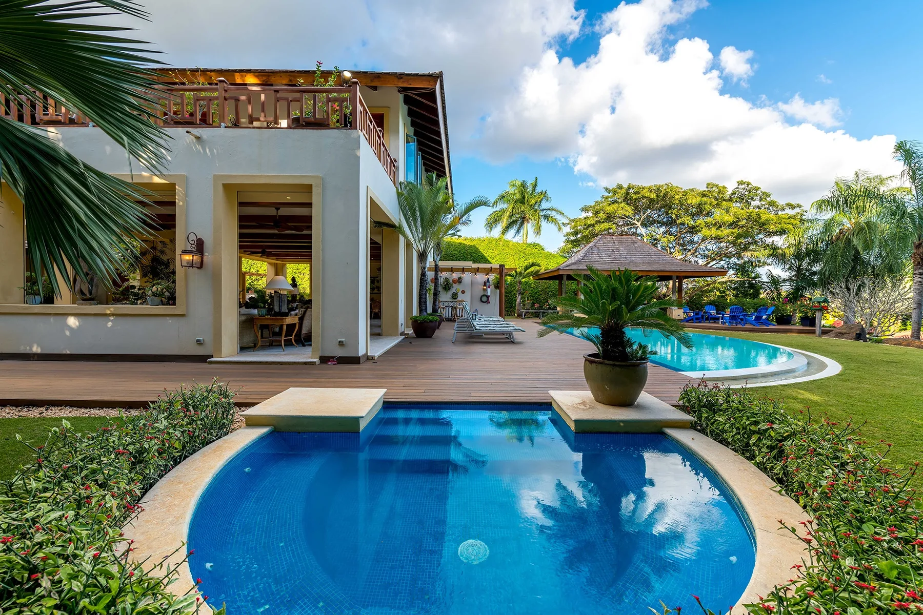 A modern house opens onto a blue swimming pool and landscaped garden.