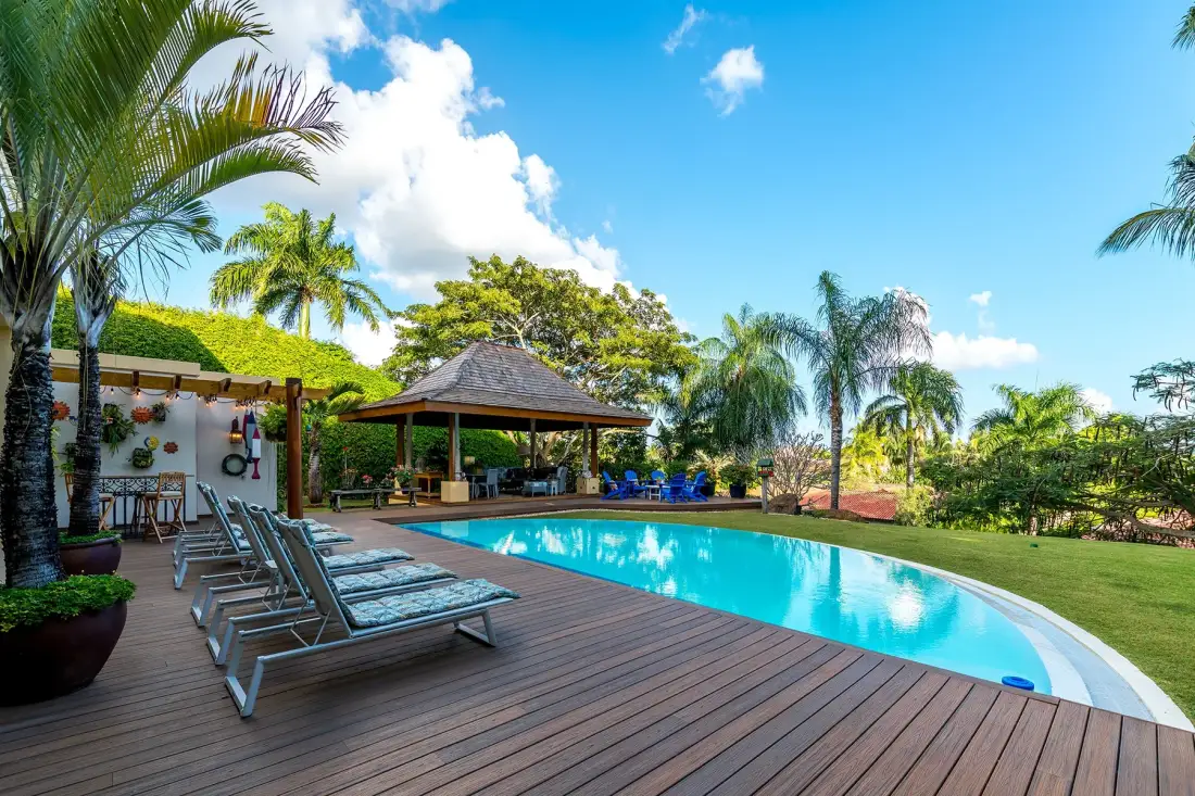 An outdoor swimming pool beside a wooden deck and shaded seating area.