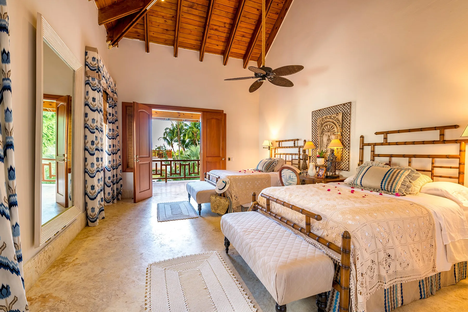 A bright bedroom with beds, patterned bedding, and a high wooden ceiling.