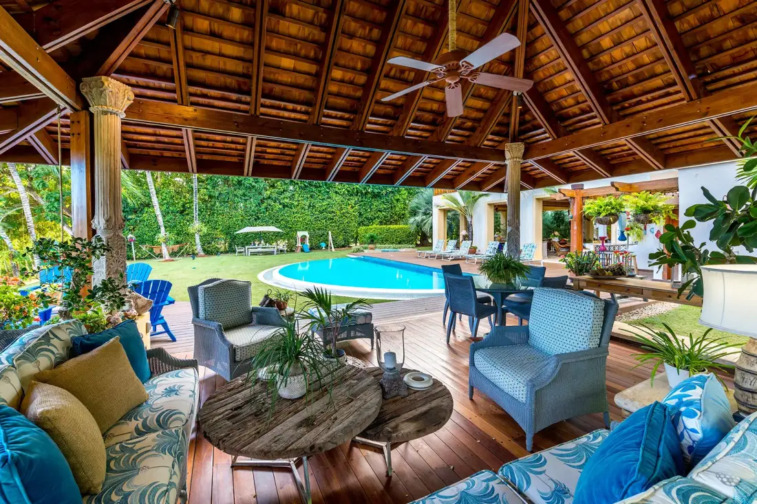 A covered outdoor seating area overlooks a swimming pool surrounded by greenery.