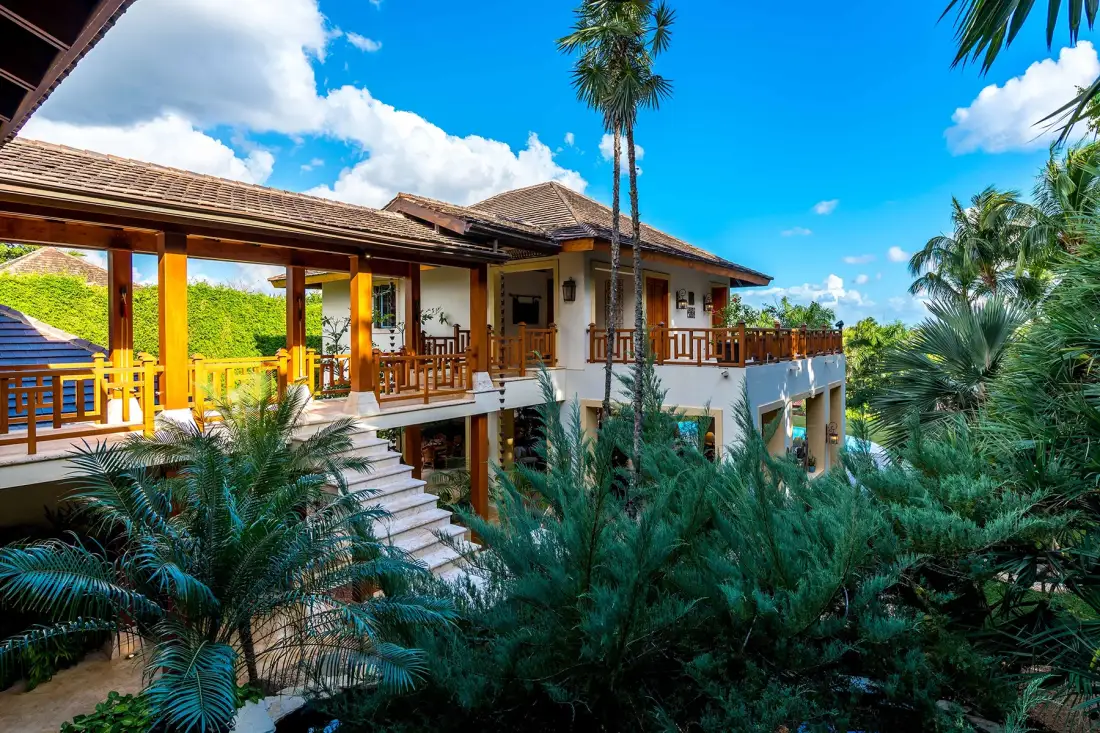 A raised tropical building with wooden balconies is surrounded by lush palms.