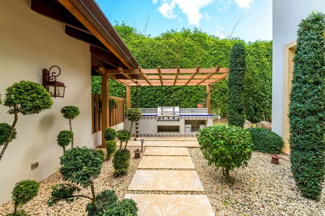 A landscaped courtyard with a stone walkway leading to a shaded outdoor kitchen.