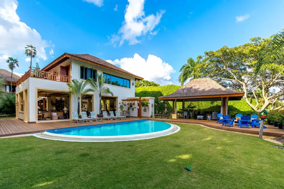 A house and covered outdoor seating area overlook a swimming pool and lawn.