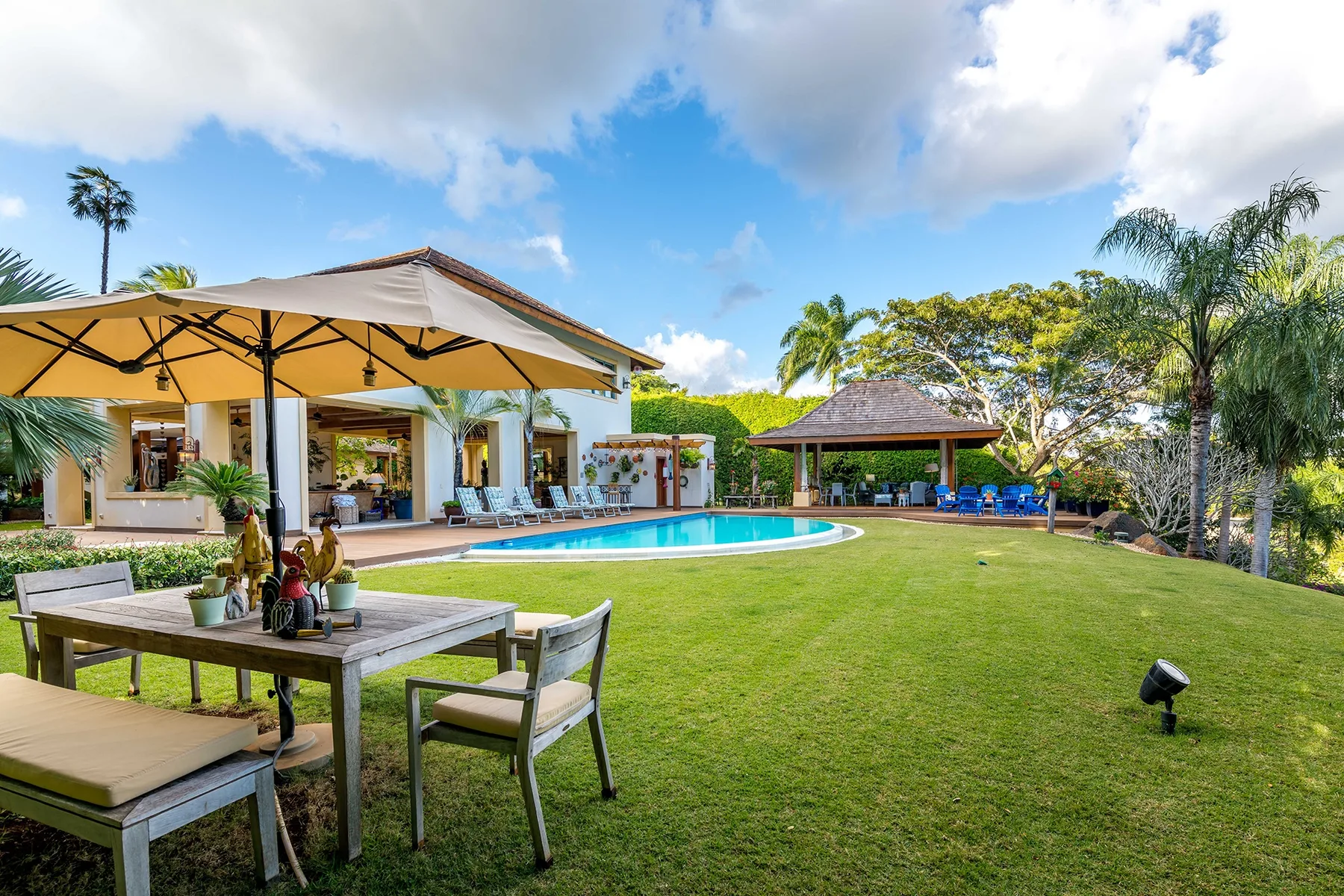 A garden patio beside a swimming pool, with outdoor seating and a shaded pavilion.