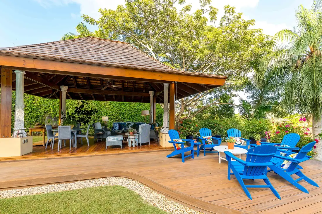 A covered outdoor seating area opens onto a wooden deck with bright blue chairs.