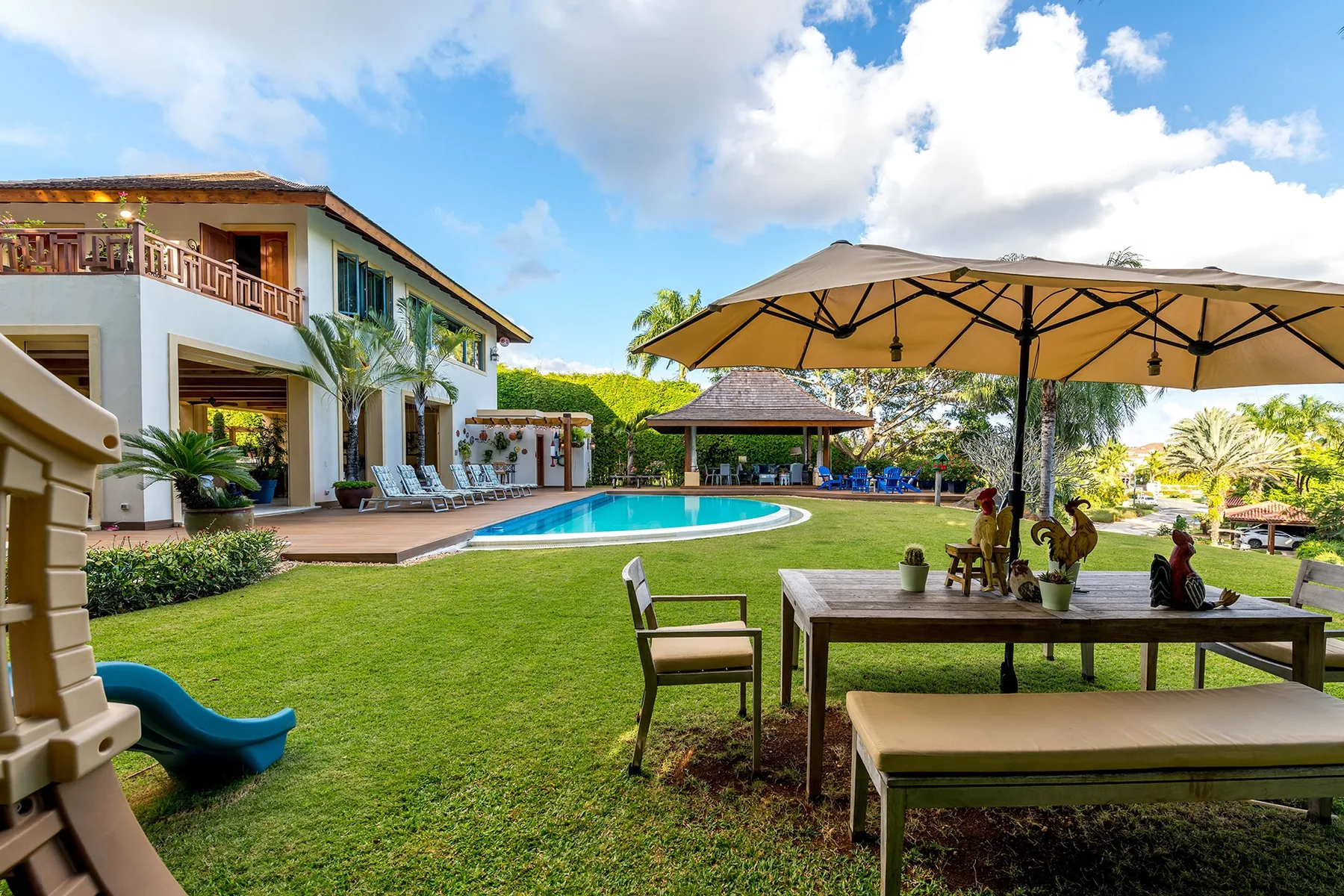 A landscaped poolside patio with outdoor seating and a large shade umbrella.