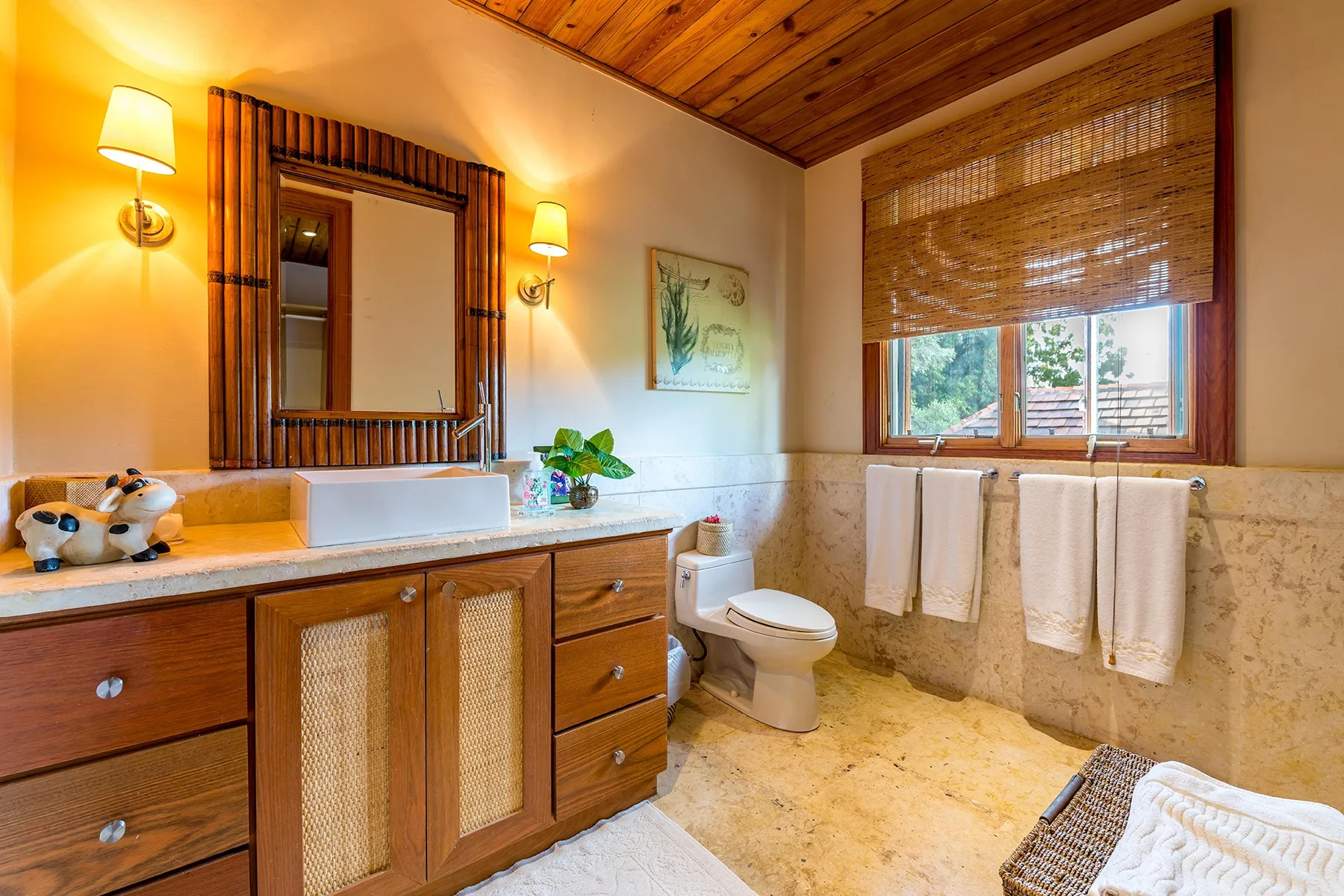 A bathroom with a wooden vanity, mirror, toilet, and window.
