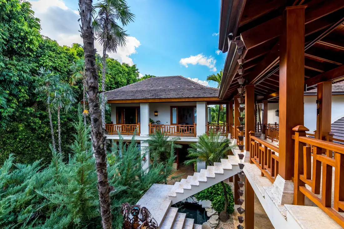 A raised building with wooden balconies and stairs sits among lush tropical greenery.