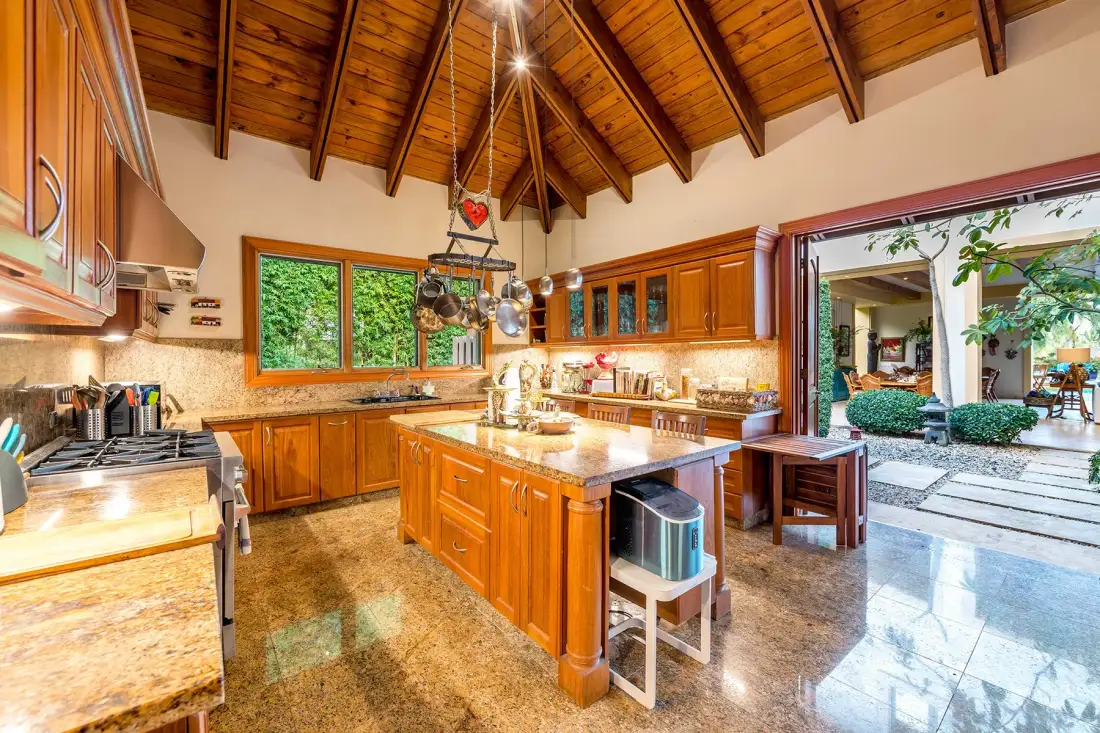 A spacious kitchen with wooden cabinets, a central island, and a high timber ceiling.