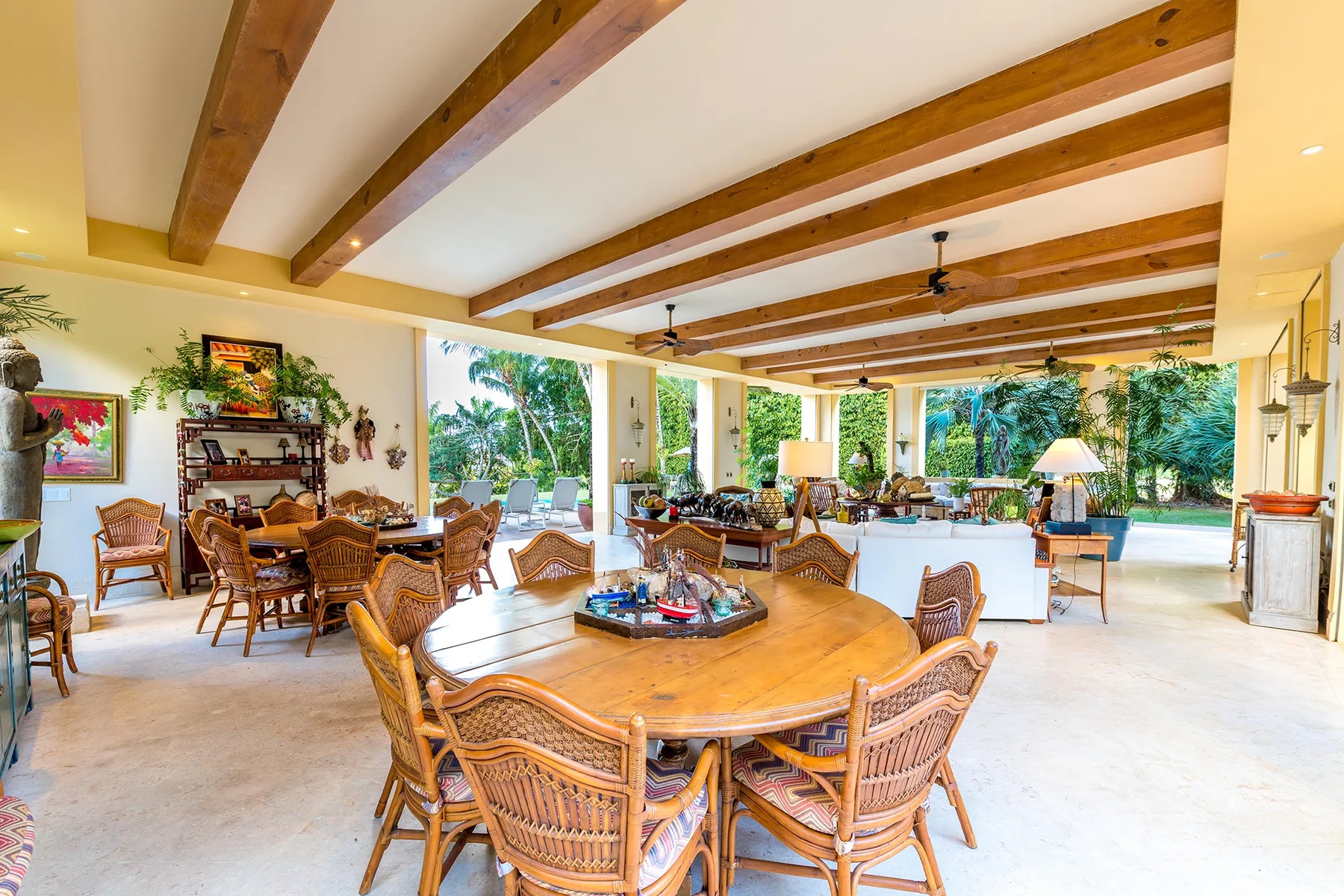 An open dining area with a large wooden table and seating, looking out onto greenery.