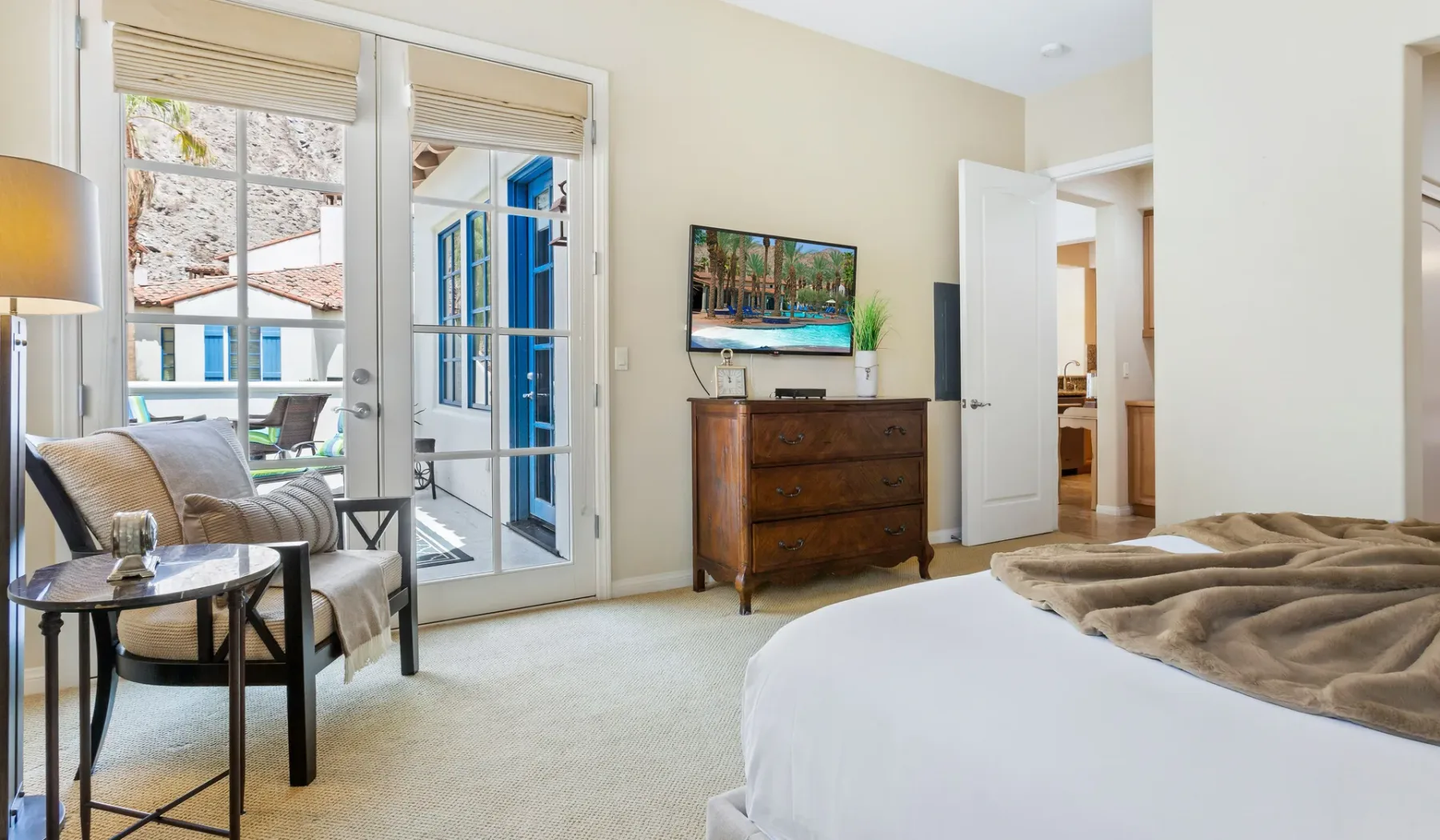 Un dormitorio con cama, zona de estar, televisor y puertas de vidrio que dan a un balcón.