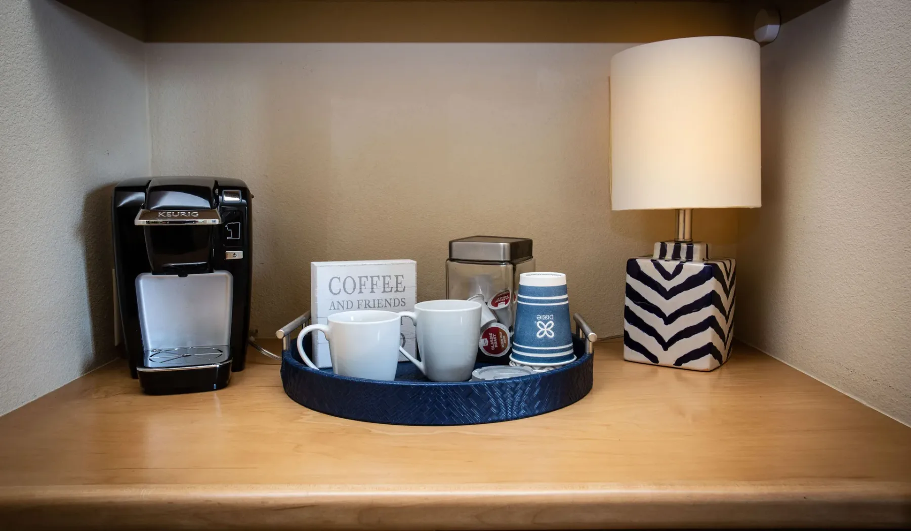 Una estación de café con cafetera, tazas y una lámpara de mesa.