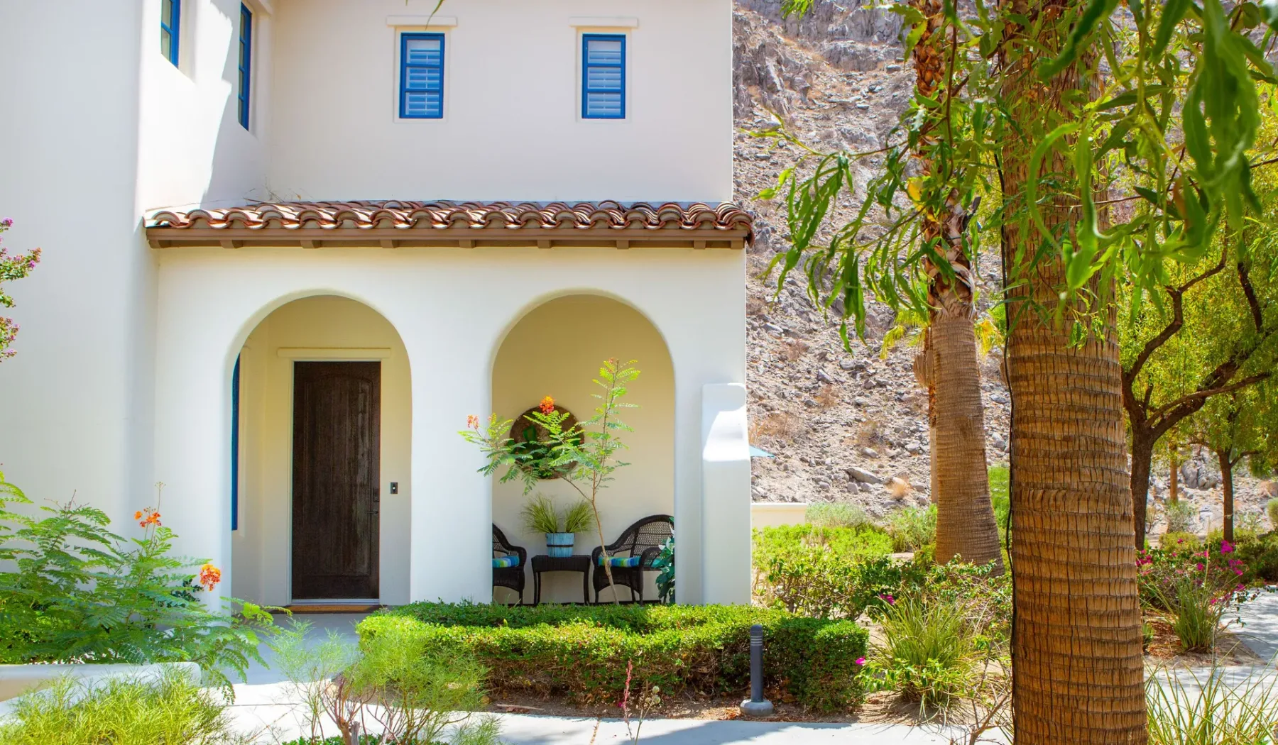 Una casa blanca de estuco tiene entradas arqueadas y un jardín con árboles.