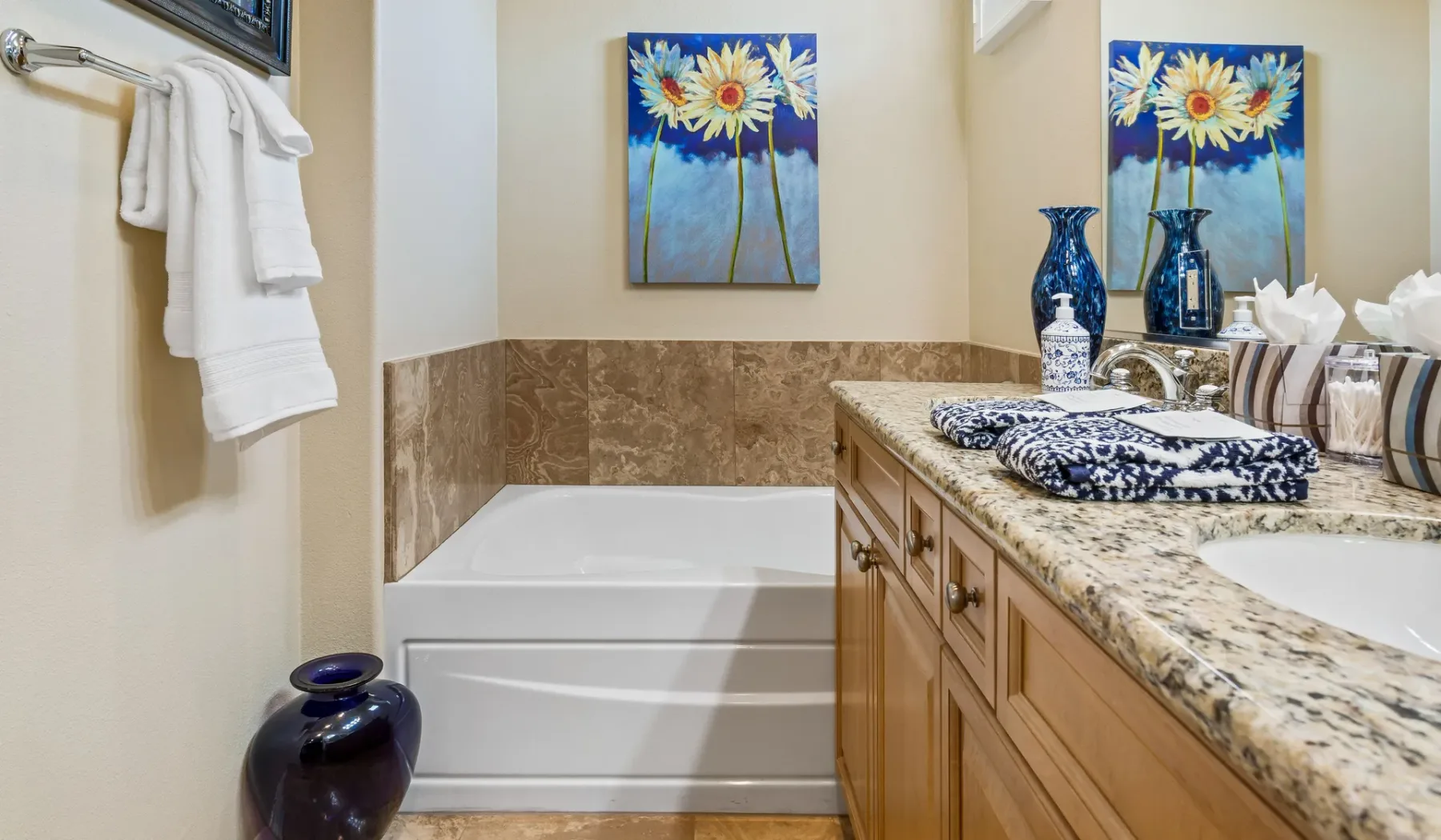 Un baño con bañera junto a un tocador largo y cuadros florales.