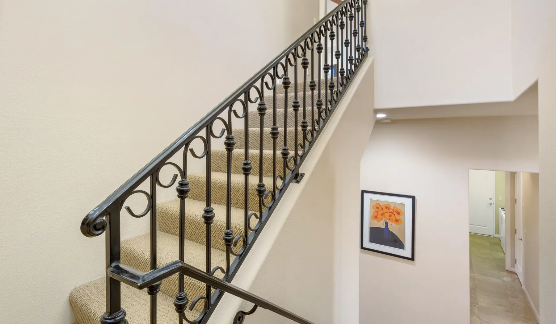 Una escalera interior con peldaños alfombrados y una barandilla metálica decorativa.