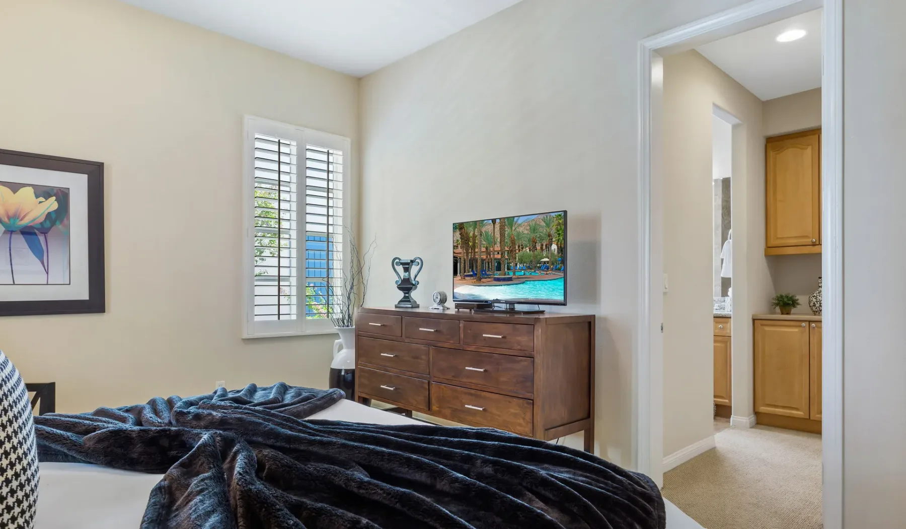 Un dormitorio con cama, cómoda y una ventana con contraventanas blancas.