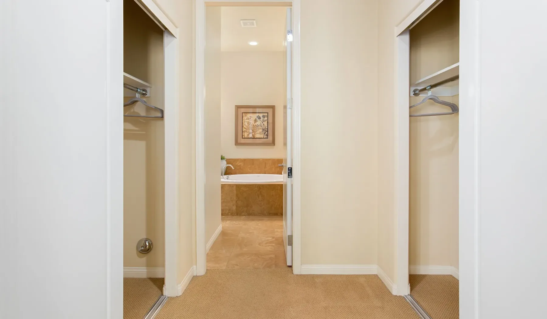 Un pasillo con armarios abiertos conduce a un baño con bañera.