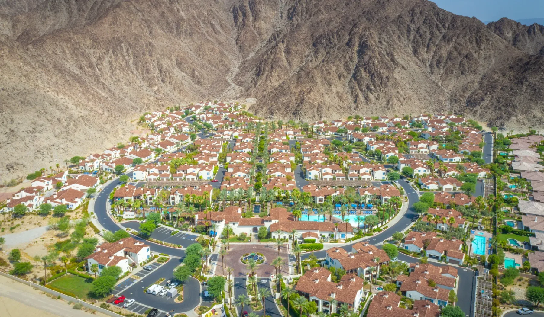 Vista aérea de un barrio residencial con tejados de tejas rojas junto a montañas escarpadas.
