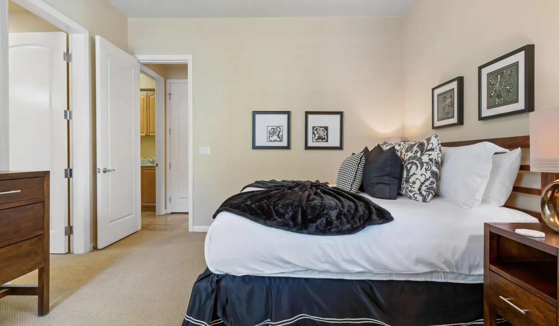 Un dormitorio con una cama, cuadros enmarcados y puertas abiertas.
