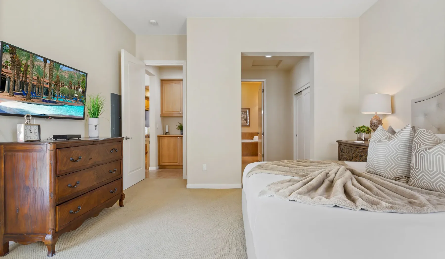 Un dormitorio luminoso con una cama, una cómoda de madera y puertas abiertas.