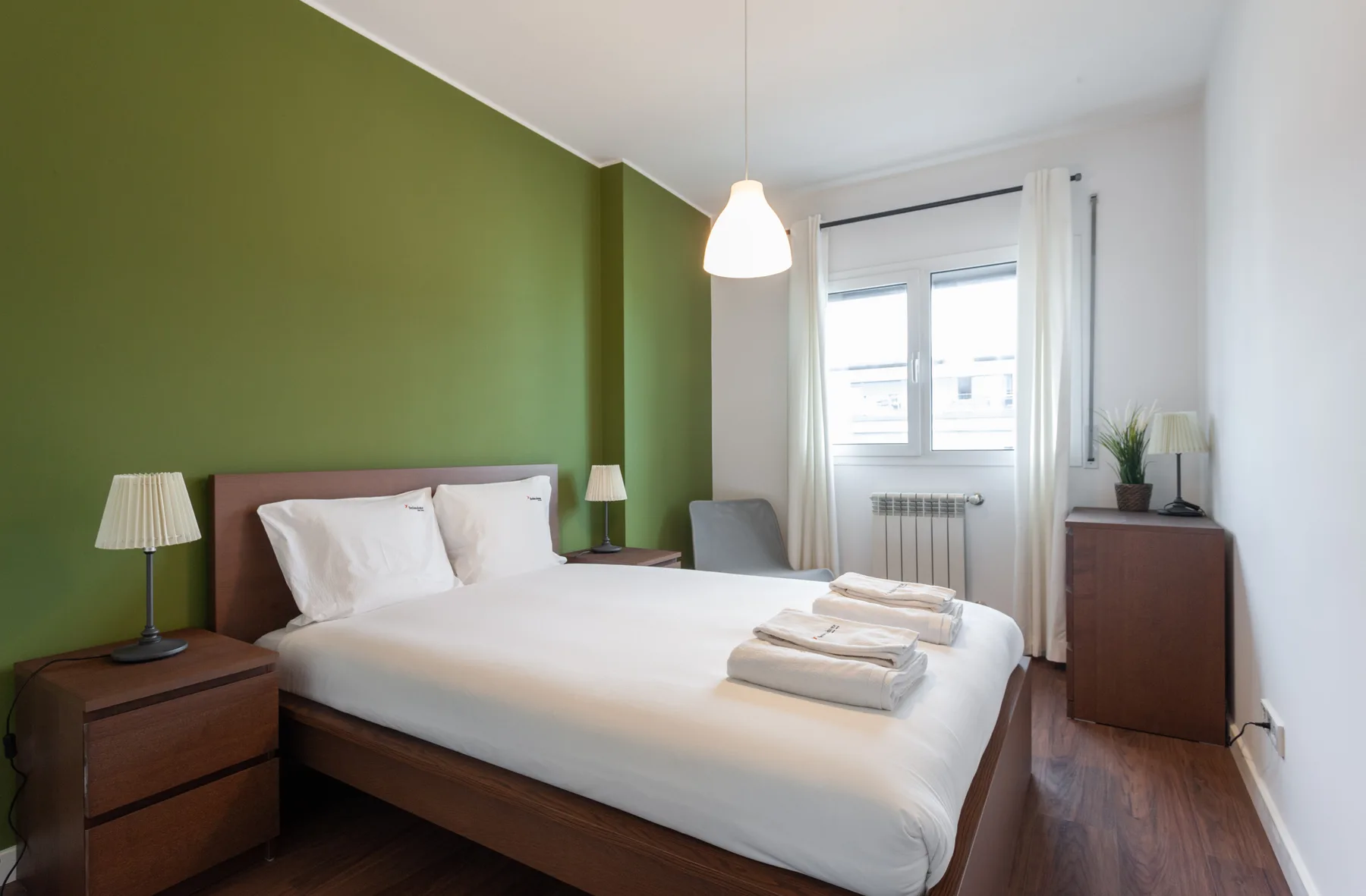A bedroom with a double bed, green accent wall, and window.