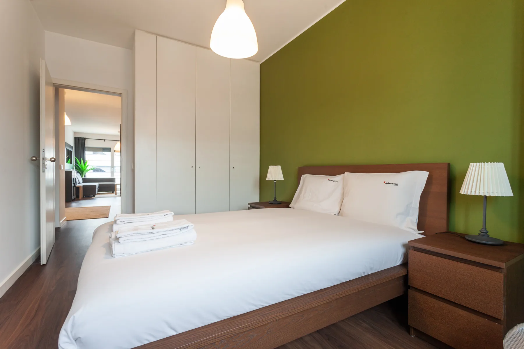 A bedroom with a neatly made bed against a green accent wall.