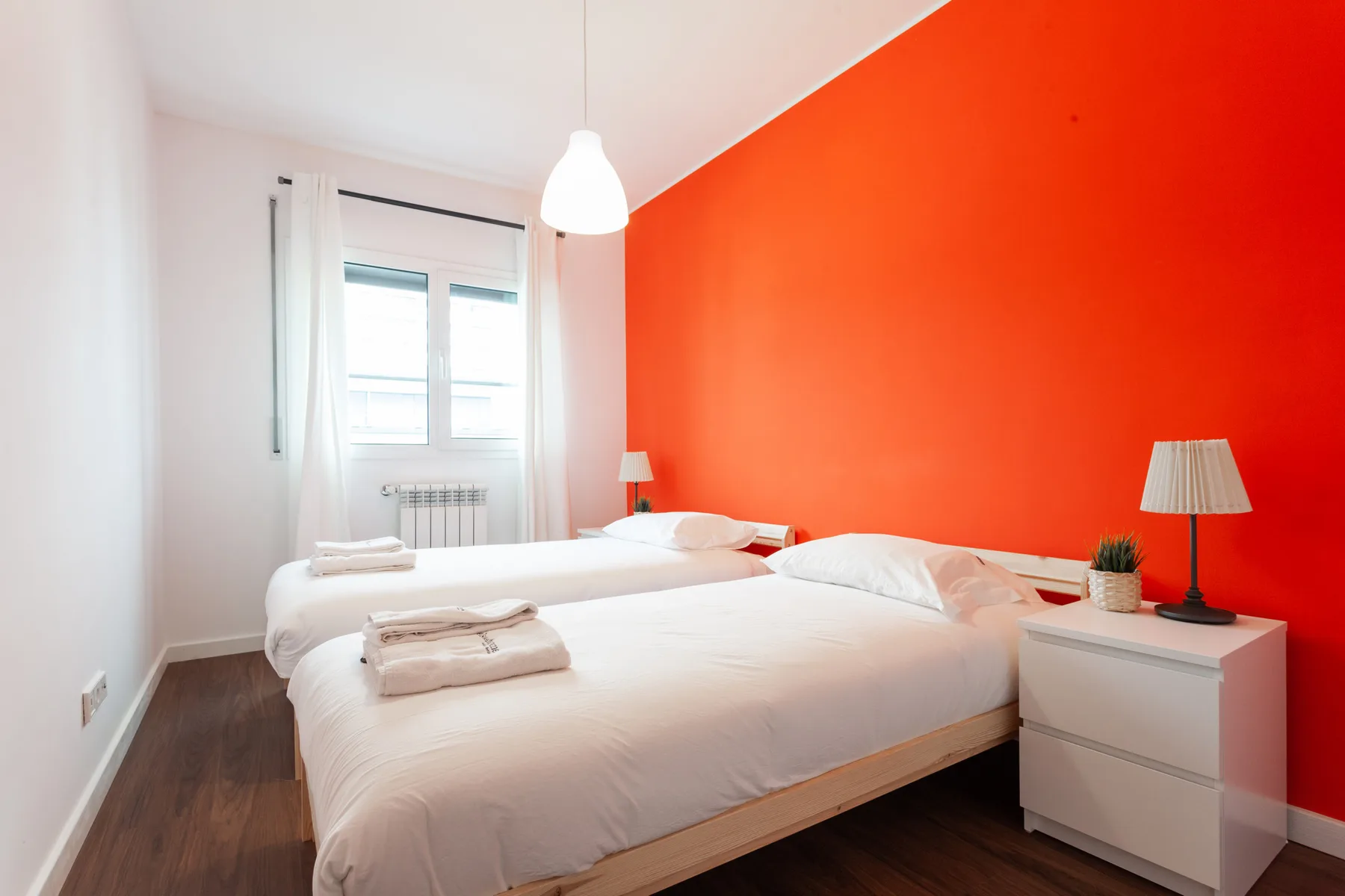 A bedroom with two beds beside a bright orange accent wall.
