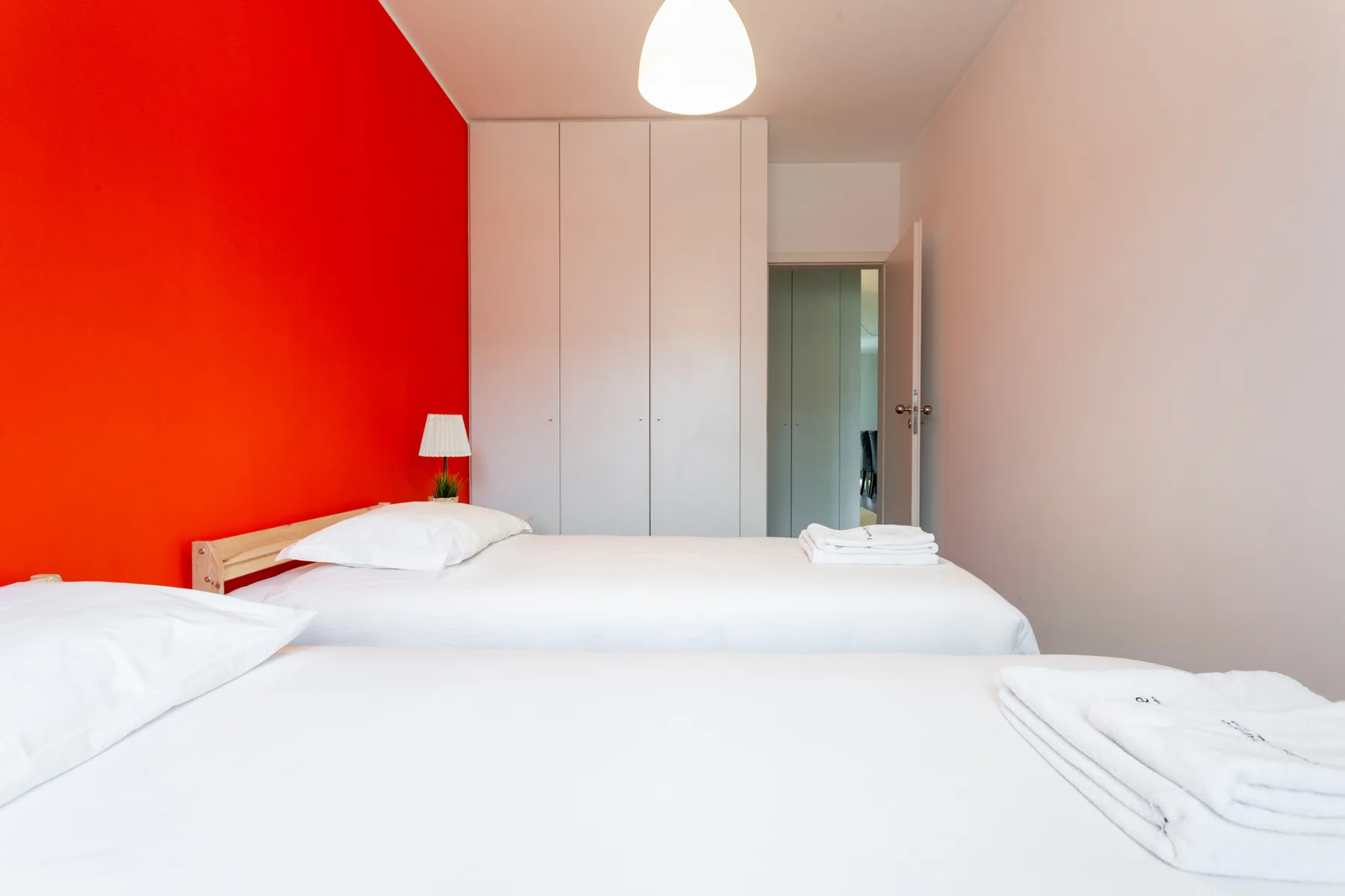 A bedroom with two beds, white bedding, and a bright red accent wall.