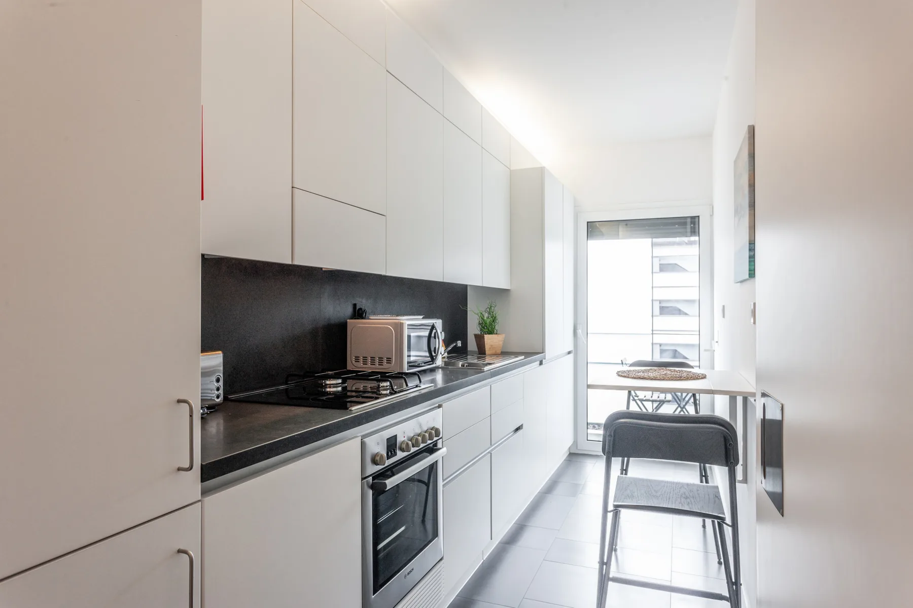 A modern kitchen with white cabinets and a dining table by the window.