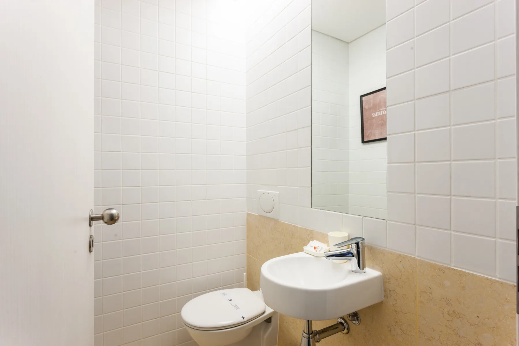 A tiled bathroom with a sink, toilet, and wall mirror.