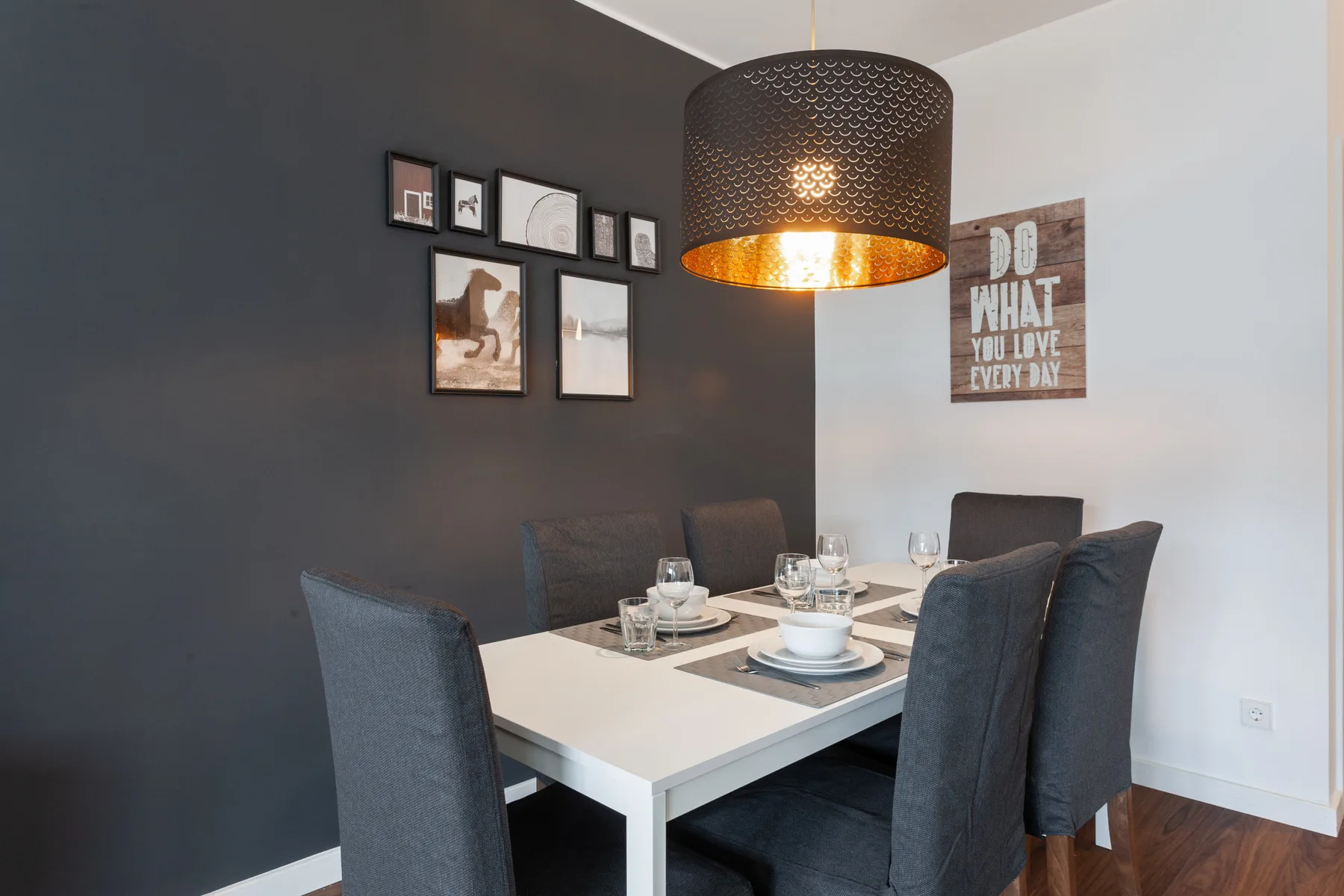A dining area with a white table and dark upholstered seating beneath a pendant light.