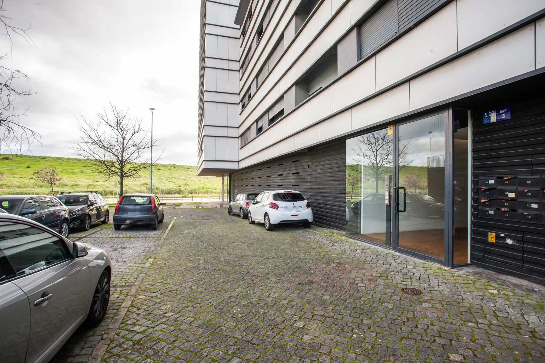A paved parking area beside a modern apartment building, with several parked cars.