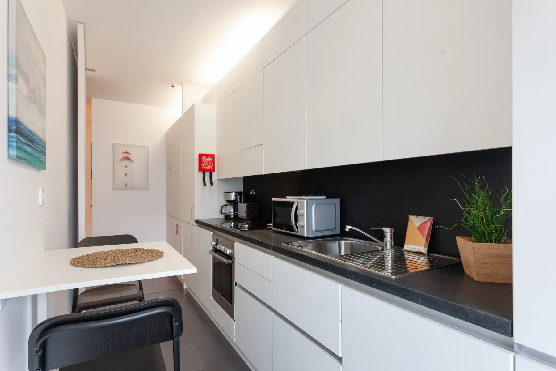 A modern kitchen with white cabinets, dark counters, and a small dining table.