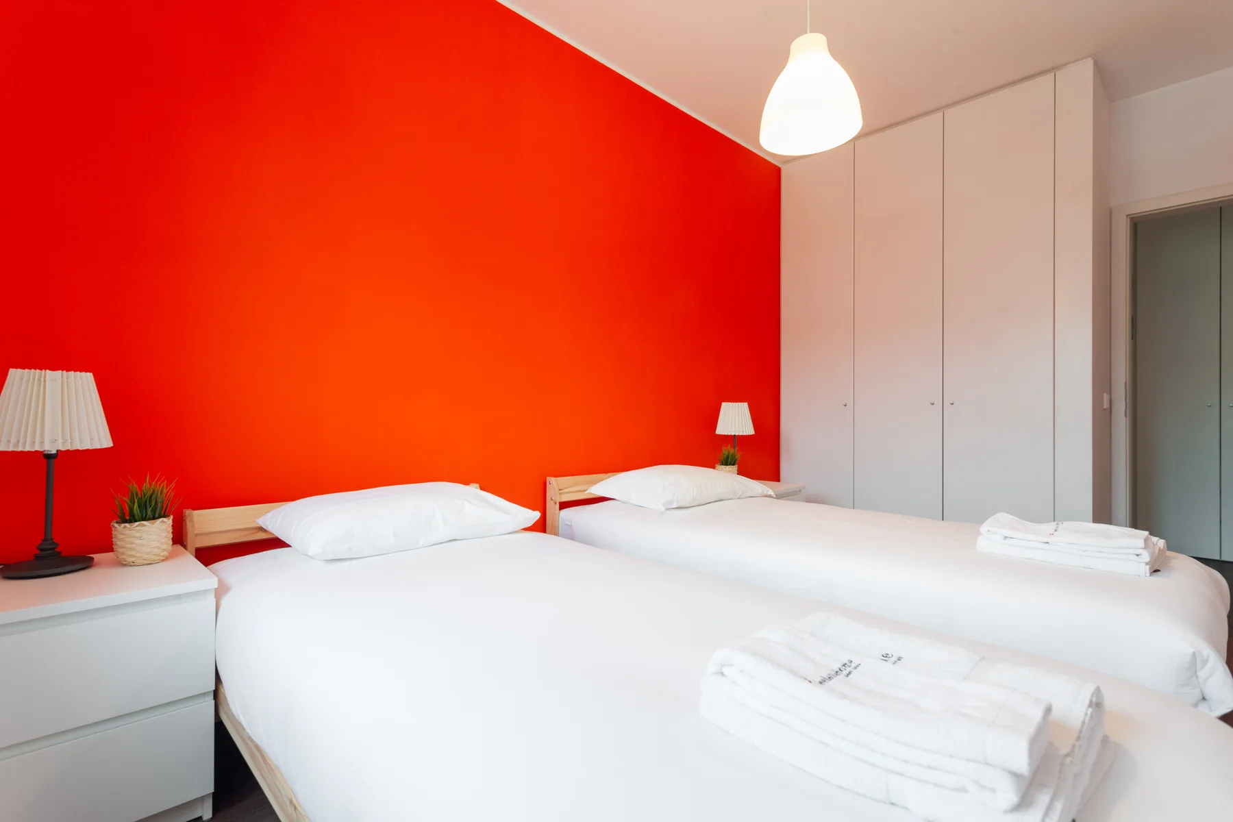 A bedroom with two beds, white bedding, and a bright red wall.