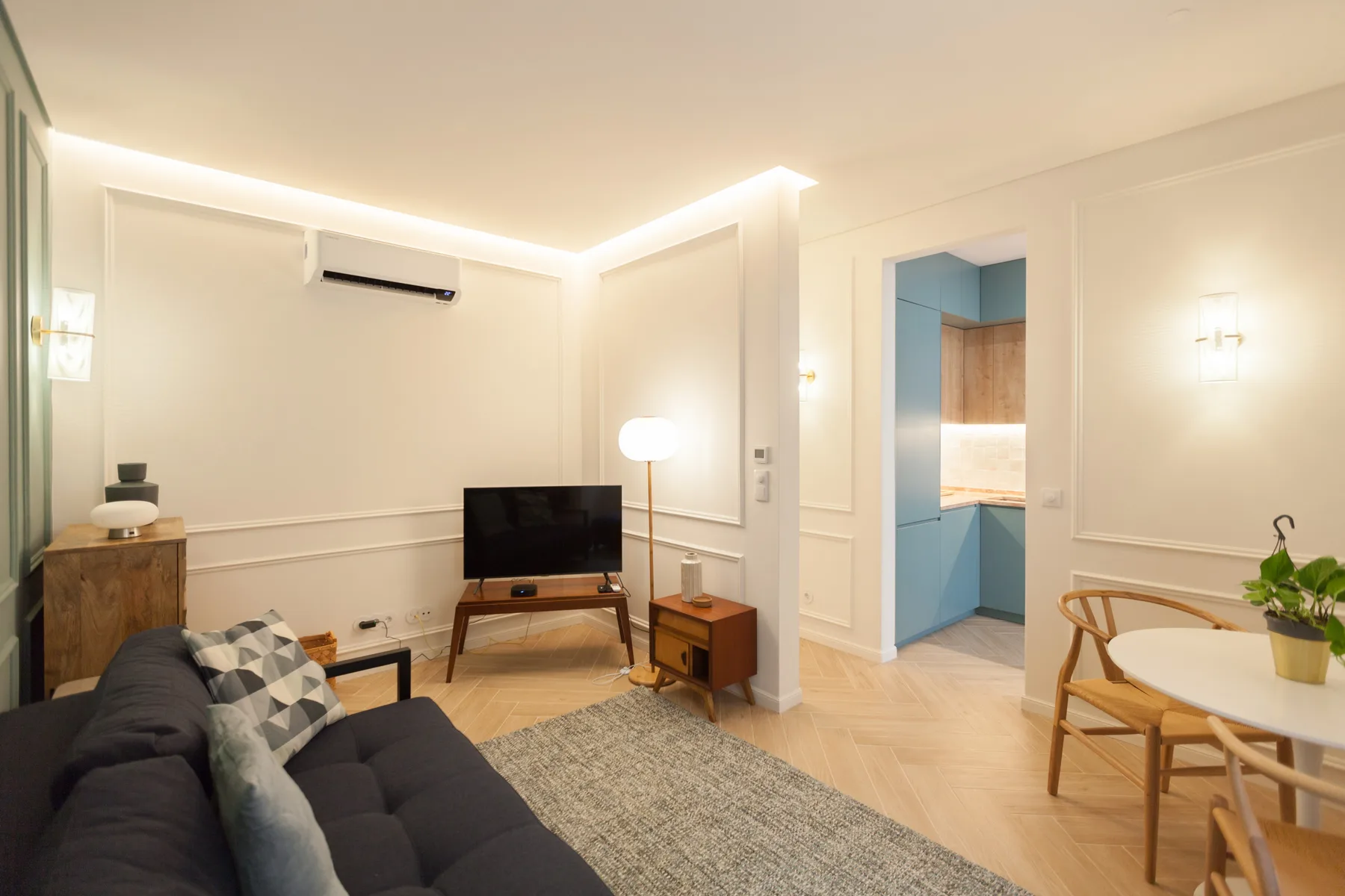Una sala de estar con asientos, un televisor y una puerta abierta a otra habitación.