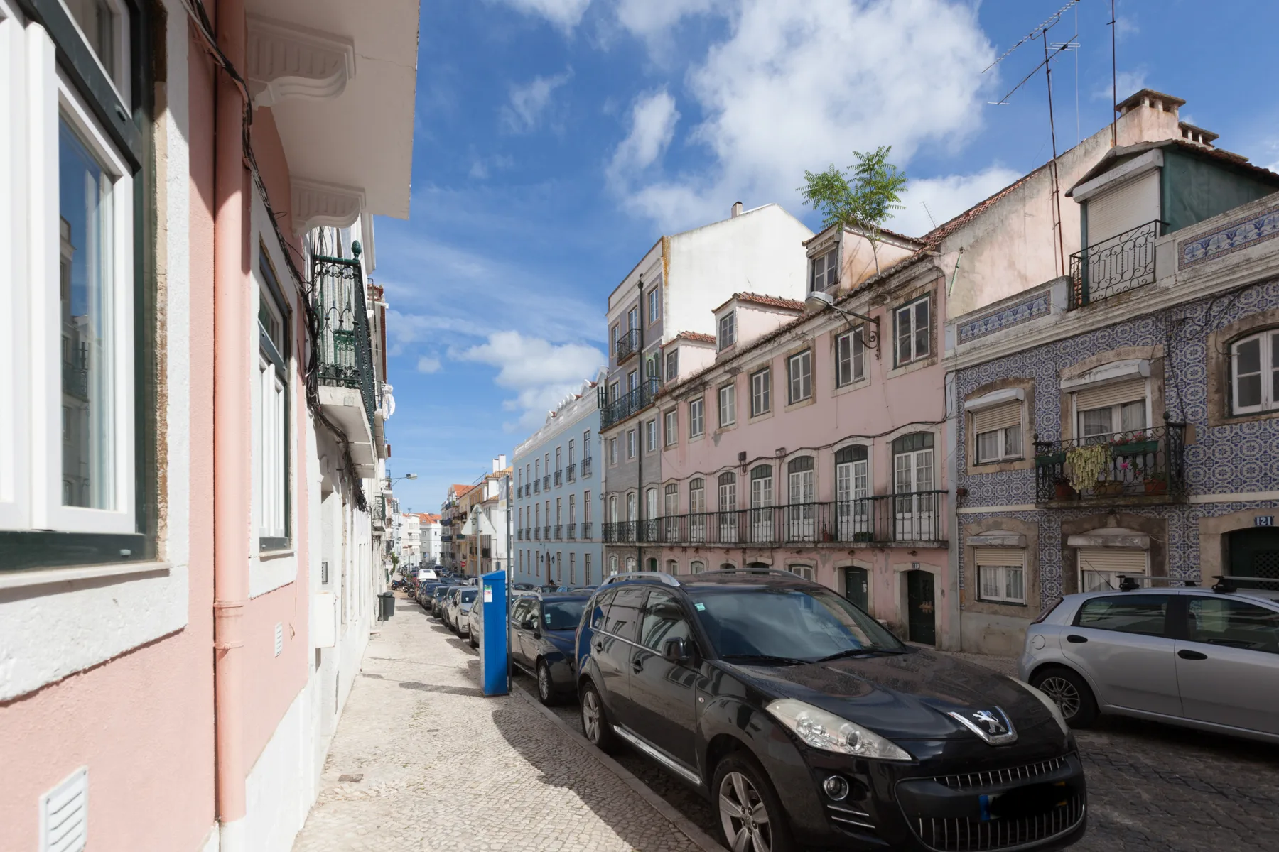 Una calle soleada con edificios de colores pastel y coches estacionados.