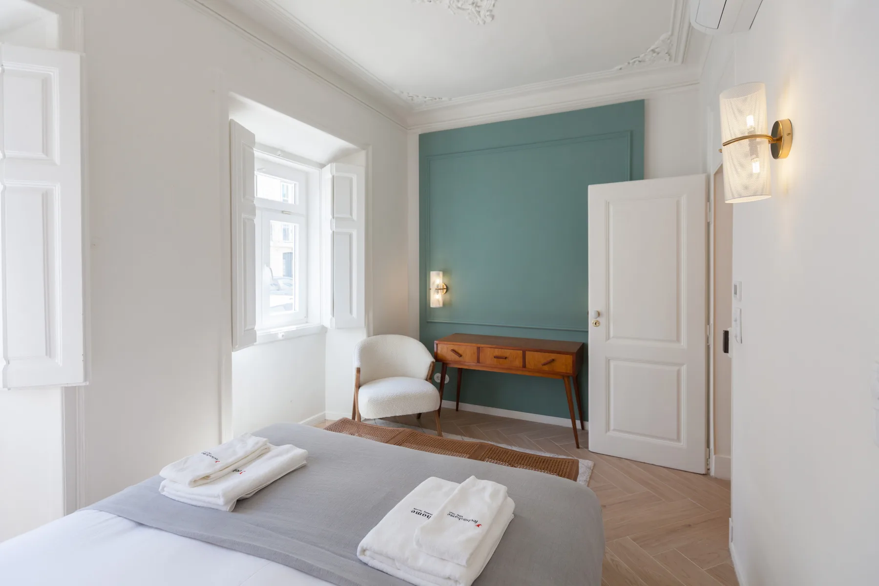Un dormitorio luminoso con una cama, una pared decorativa verde azulado y un escritorio.