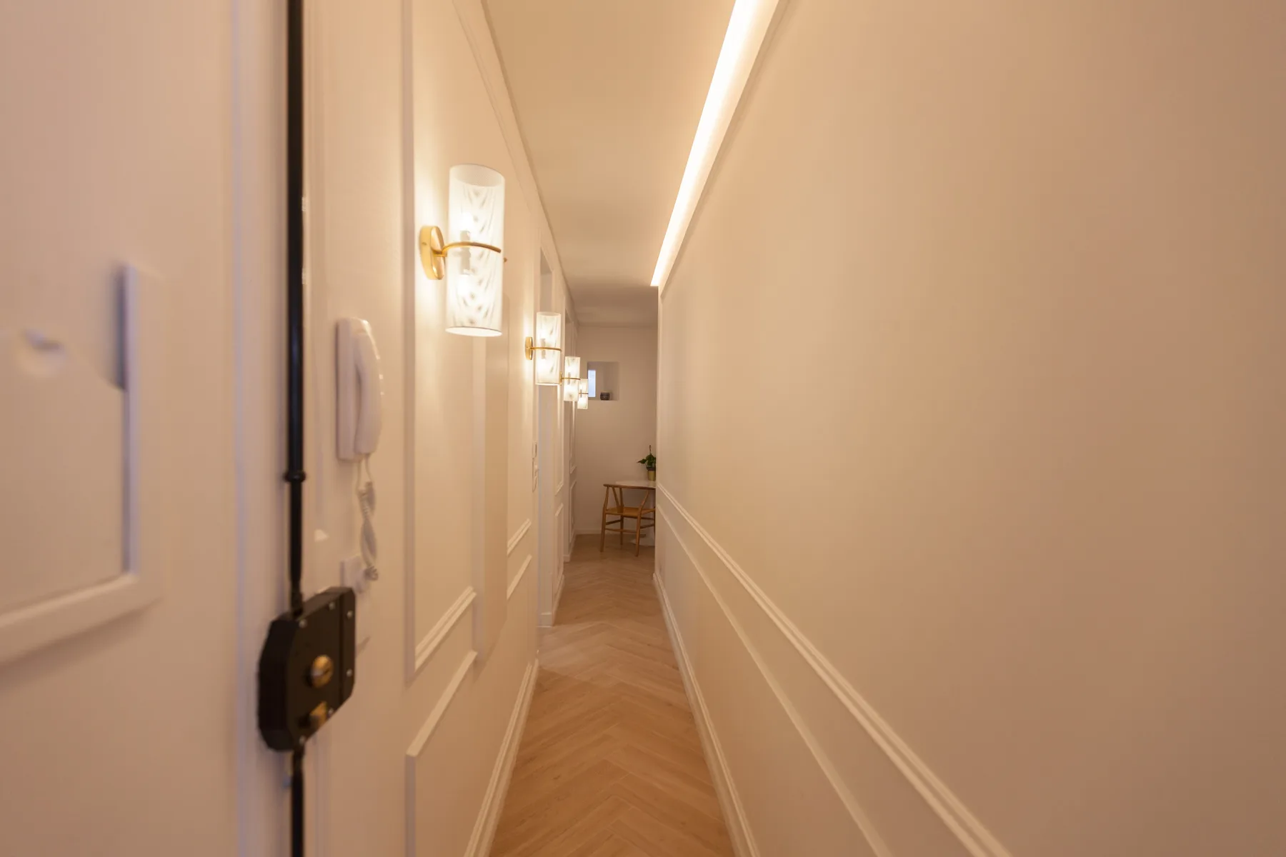 Un pasillo estrecho con apliques de pared y suelo de madera clara.