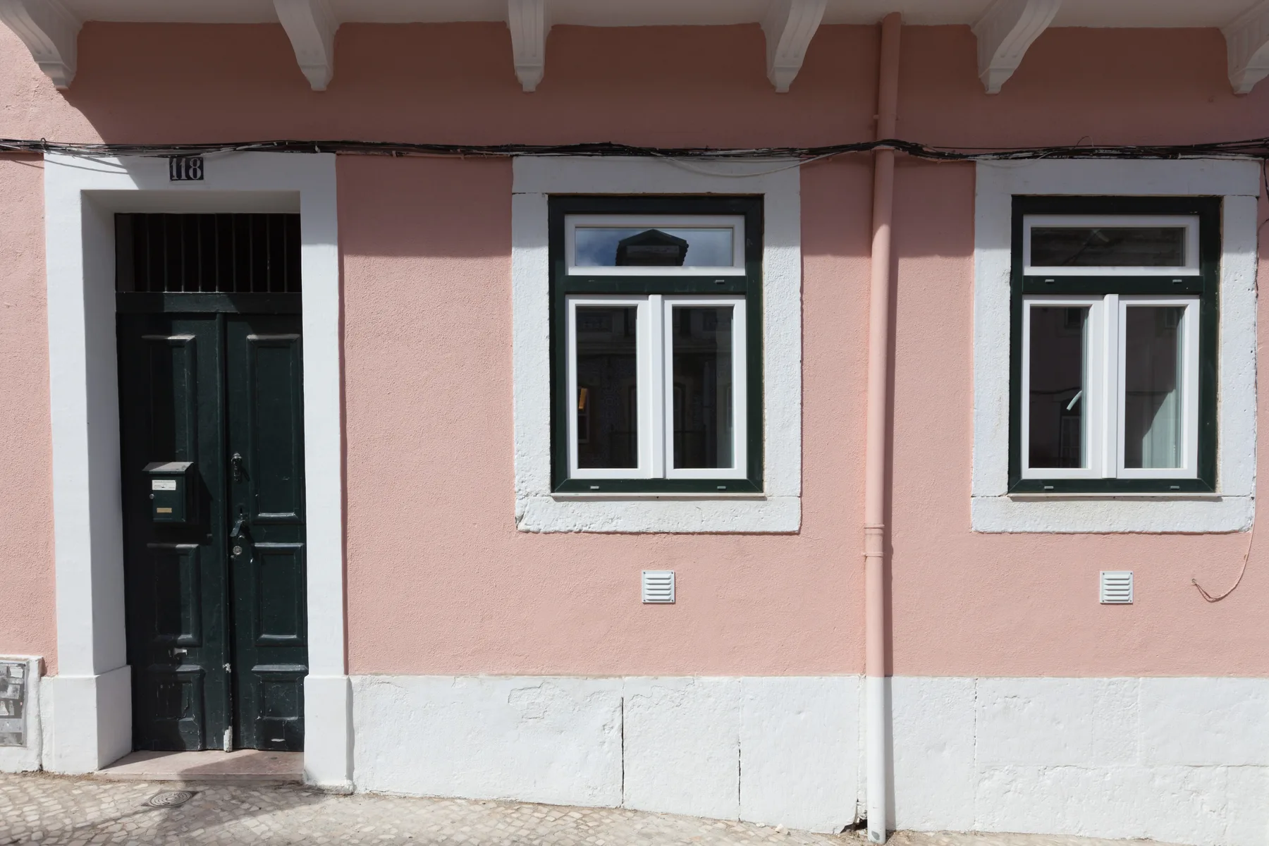 Una fachada rosa con una puerta oscura y dos ventanas.