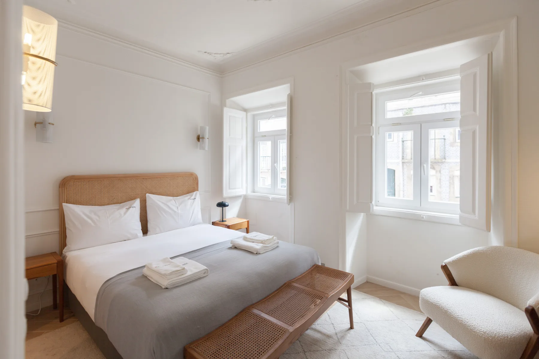 Un dormitorio luminoso con una cama doble, un banco y ventanas grandes.