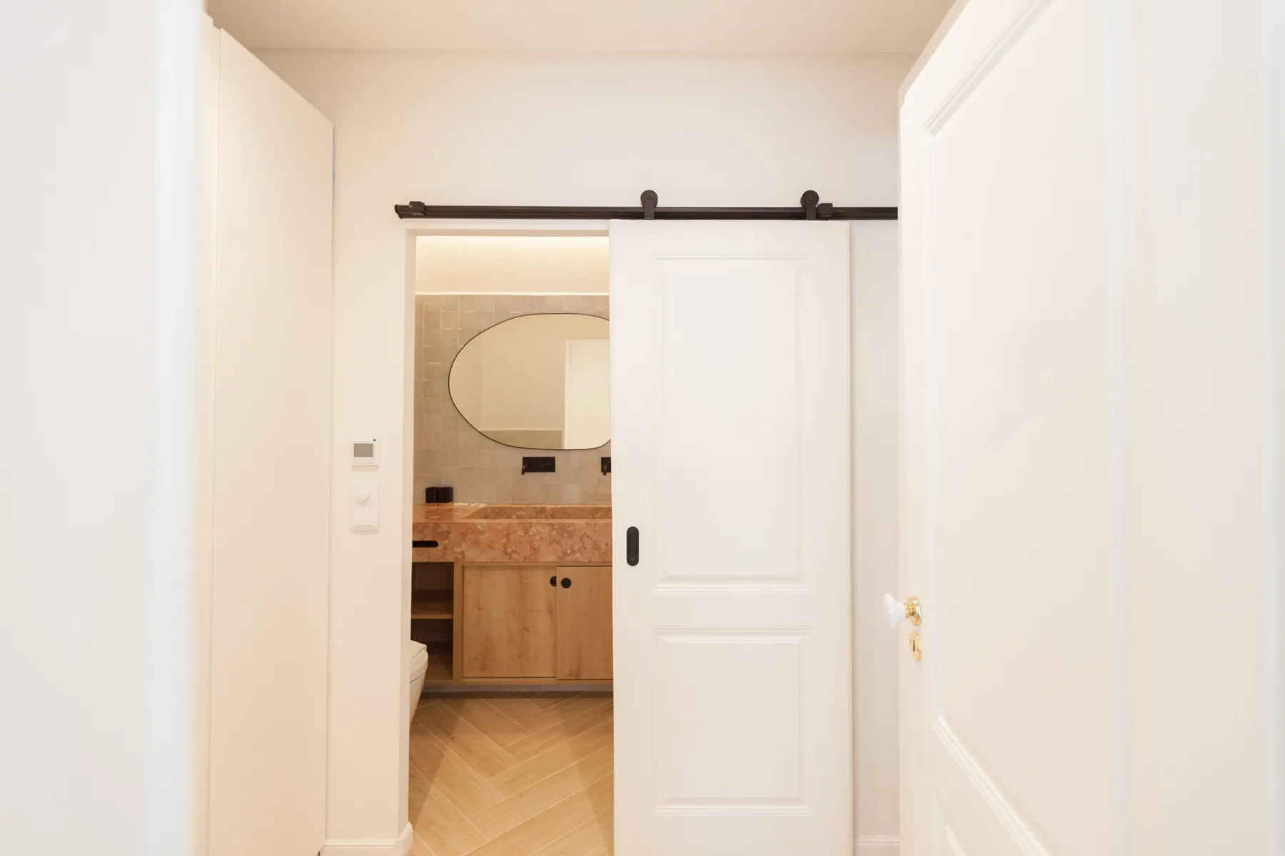 Se ve un lavabo de baño y un espejo ovalado a través de una puerta corredera parcialmente abierta.