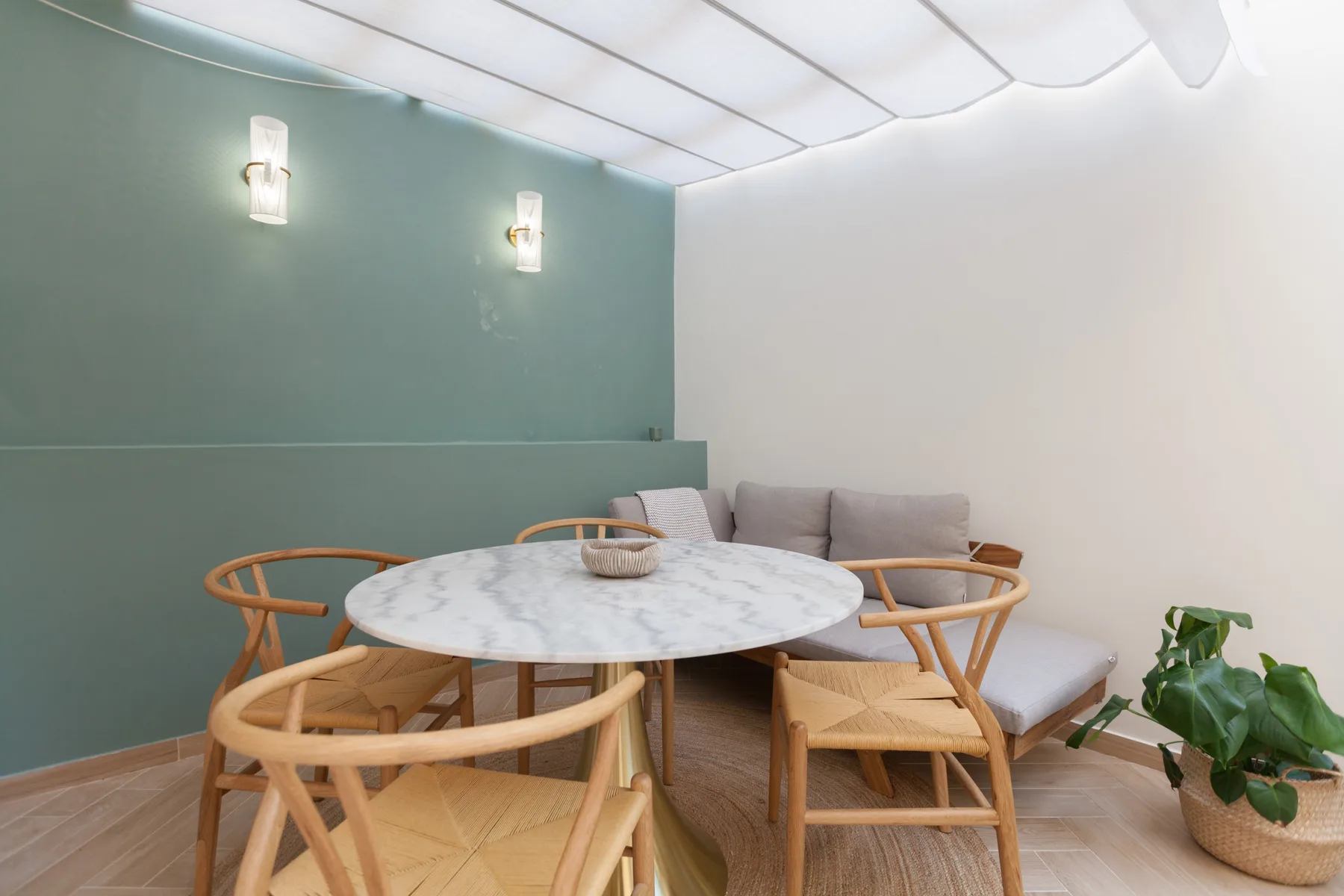 Un rincón de comedor con una mesa redonda, asientos de madera y una planta en maceta.