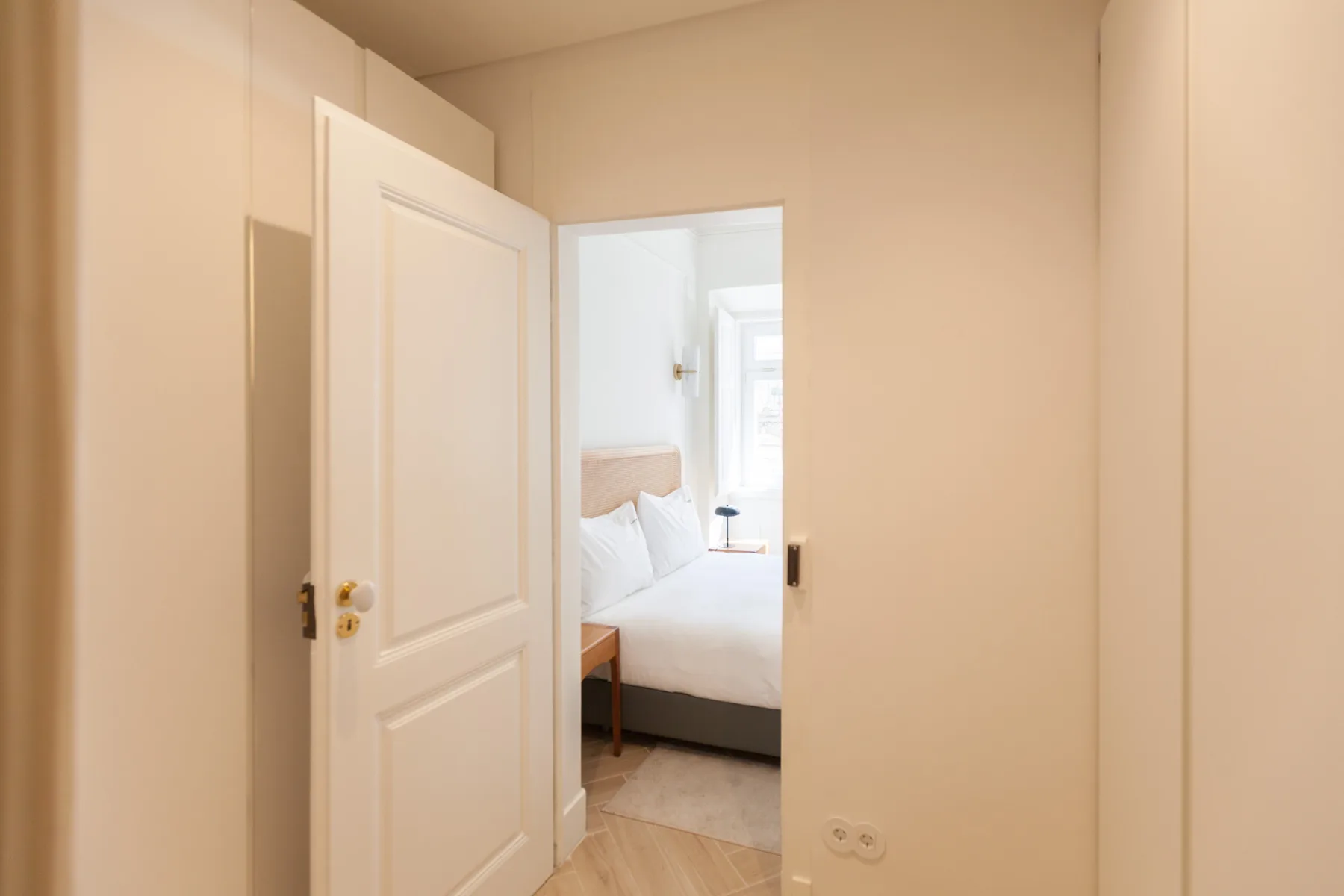 Un pasillo da a un dormitorio luminoso con una cama.