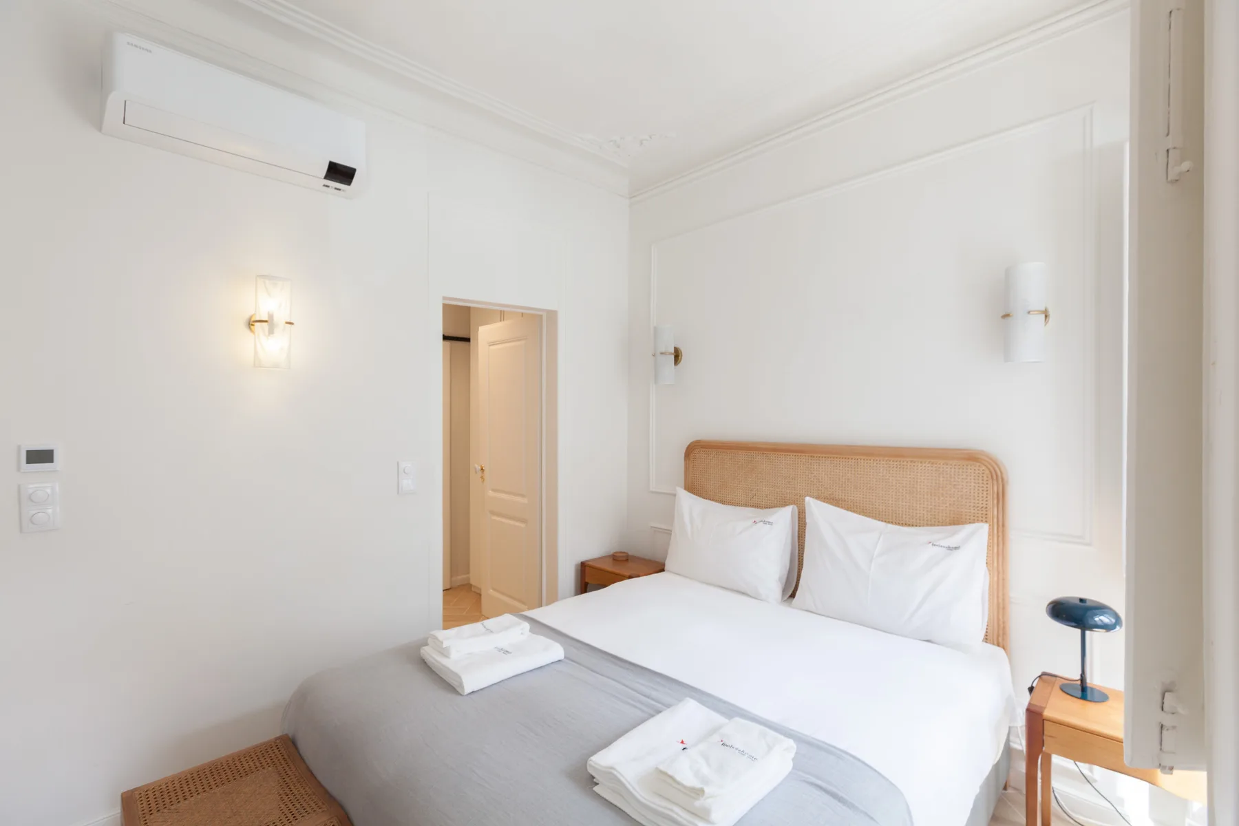 Un dormitorio luminoso con cama, cabecero tejido y mesitas de noche.