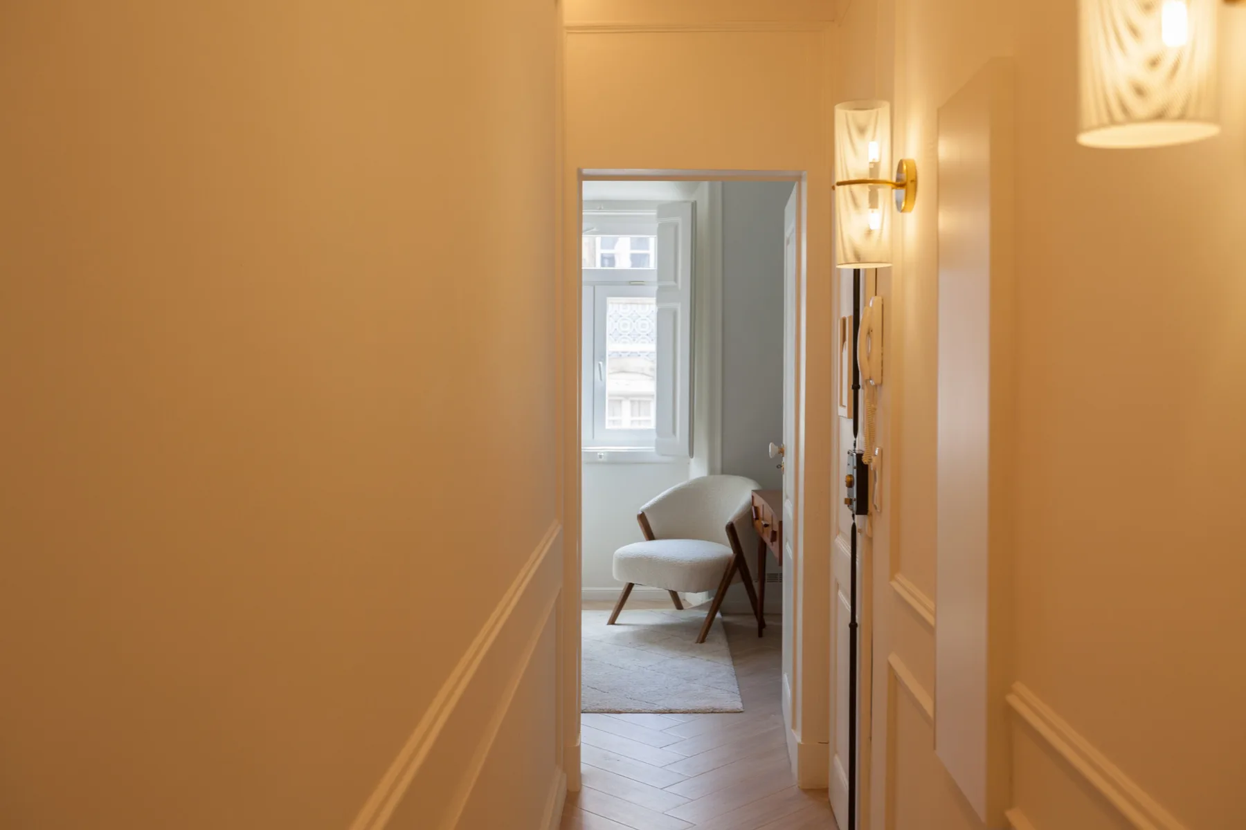 Un pasillo estrecho conduce a una habitación luminosa con una silla y una ventana.
