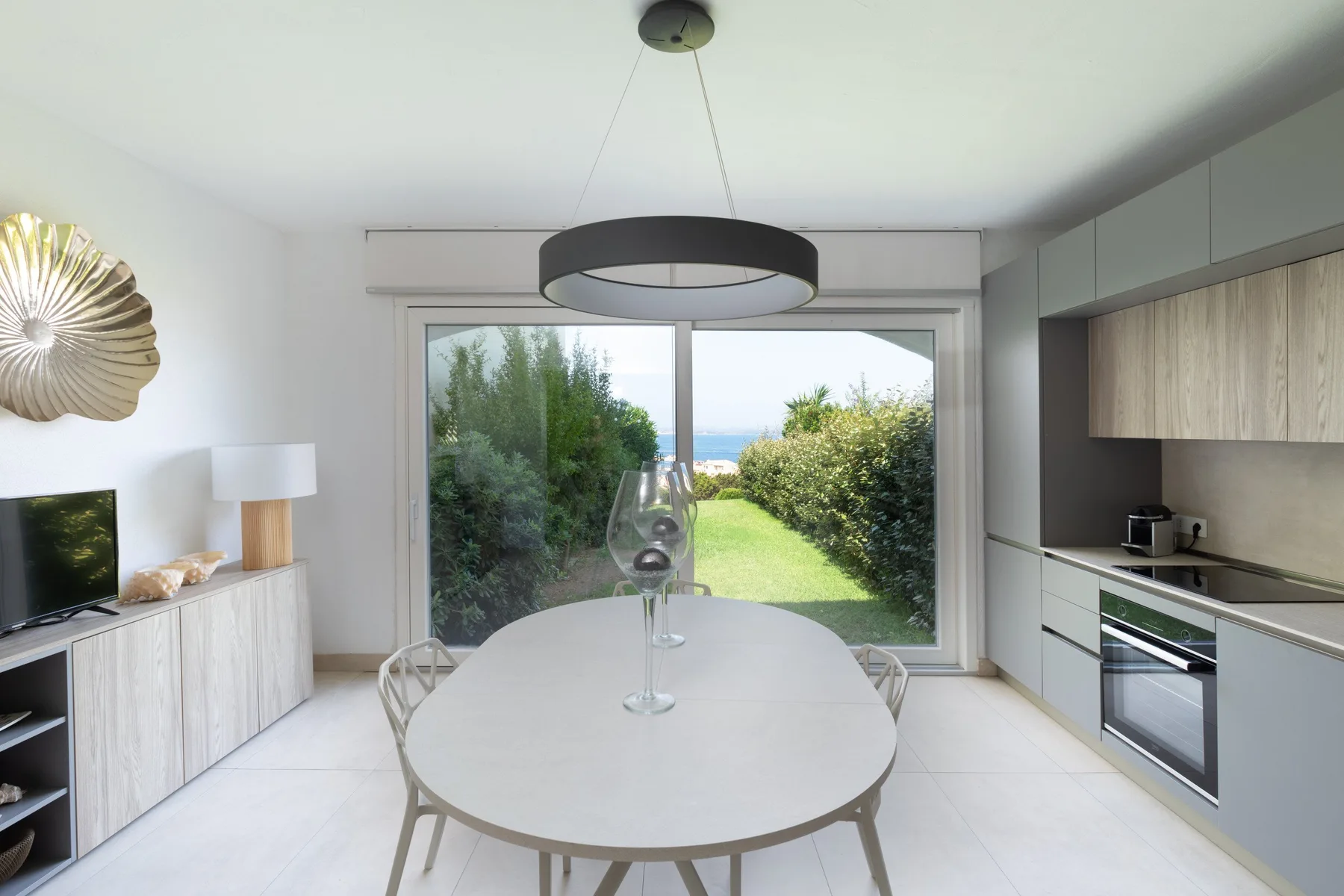 Un comedor luminoso con una mesa blanca y grandes ventanales con vistas a un jardín.